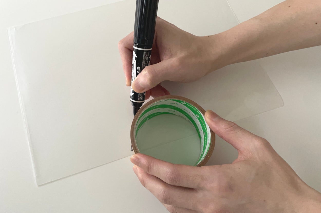 手にテープとマーカーを持ち、プラスチック表面に何かを書いている様子。