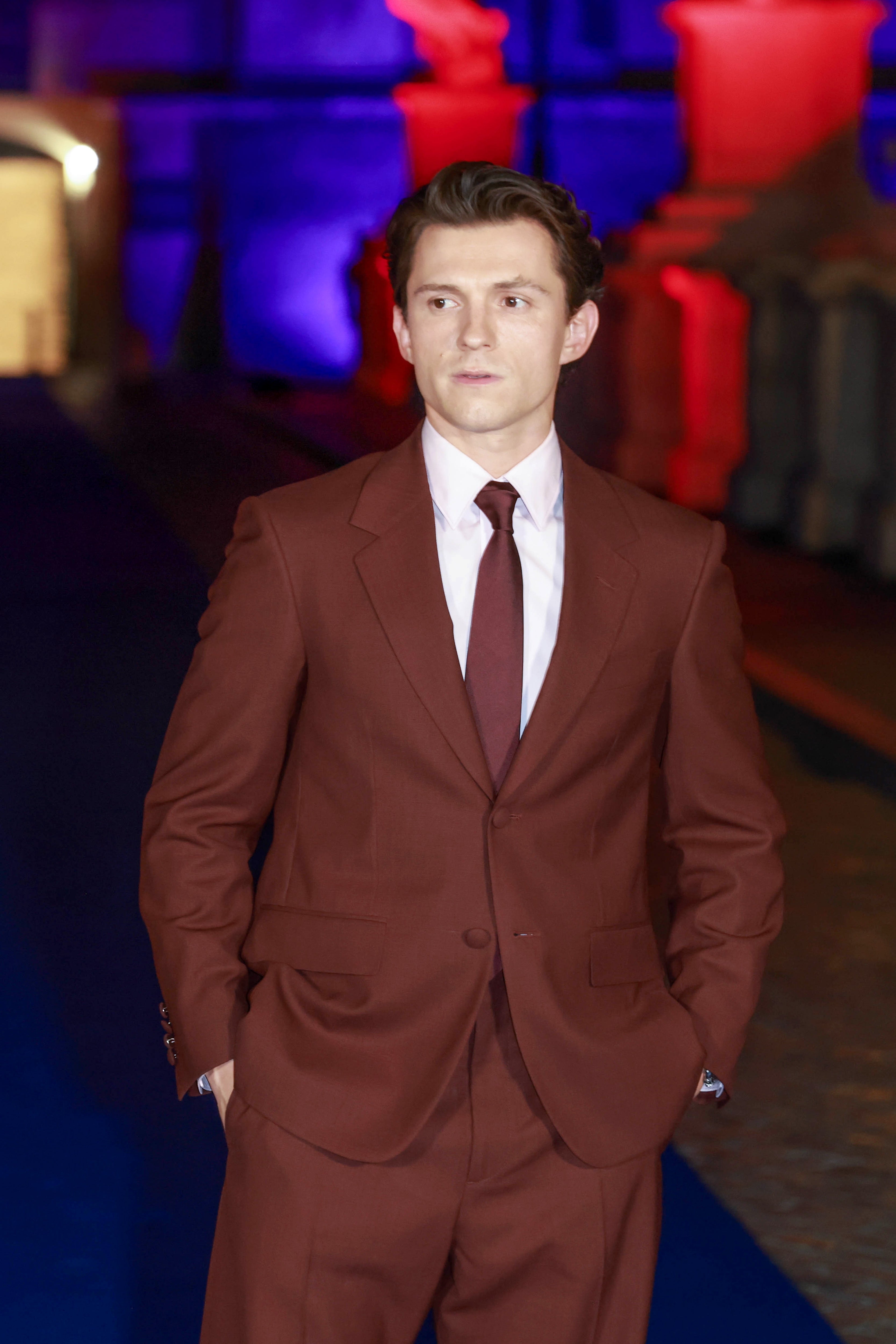 A person in a stylish suit poses on a formal event carpet