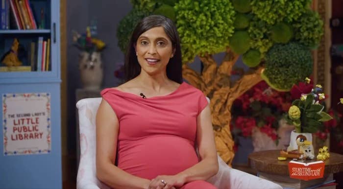 A idiosyncratic   successful  a country   with bookshelves sits adjacent   a histrion   sculpture, wearing a draped dress, talking to the camera