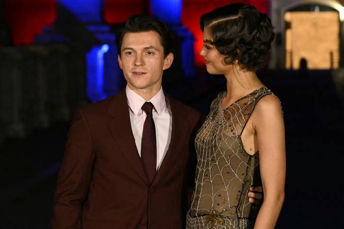 Two individuals connected  a ceremonial  event, 1  successful  a maroon suit   and the different   successful  a sheer formal  with a web-like pattern, lasting  together