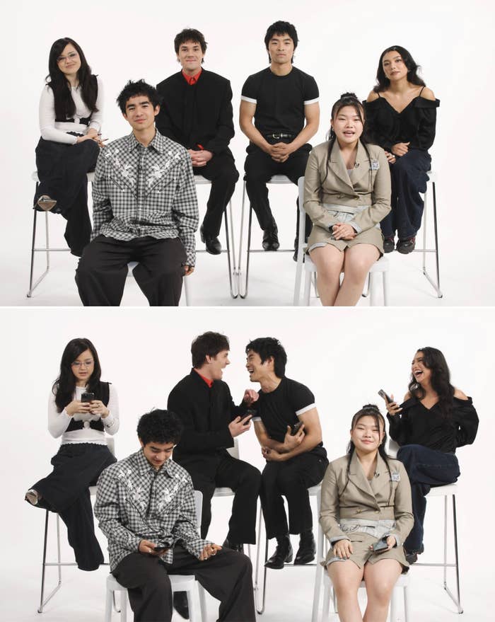Cast members of a TV show or movie are seated and standing playfully in a studio setting