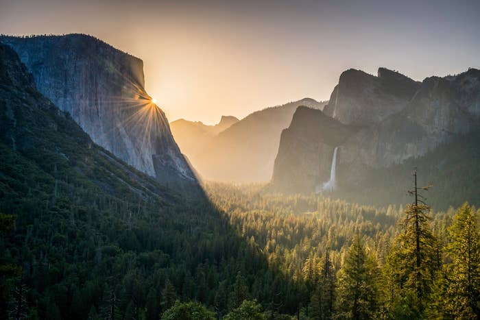 Sunrise implicit    Yosemite Valley with sunlight streaming betwixt  mountains and a distant   waterfall, highlighting the scenic landscape