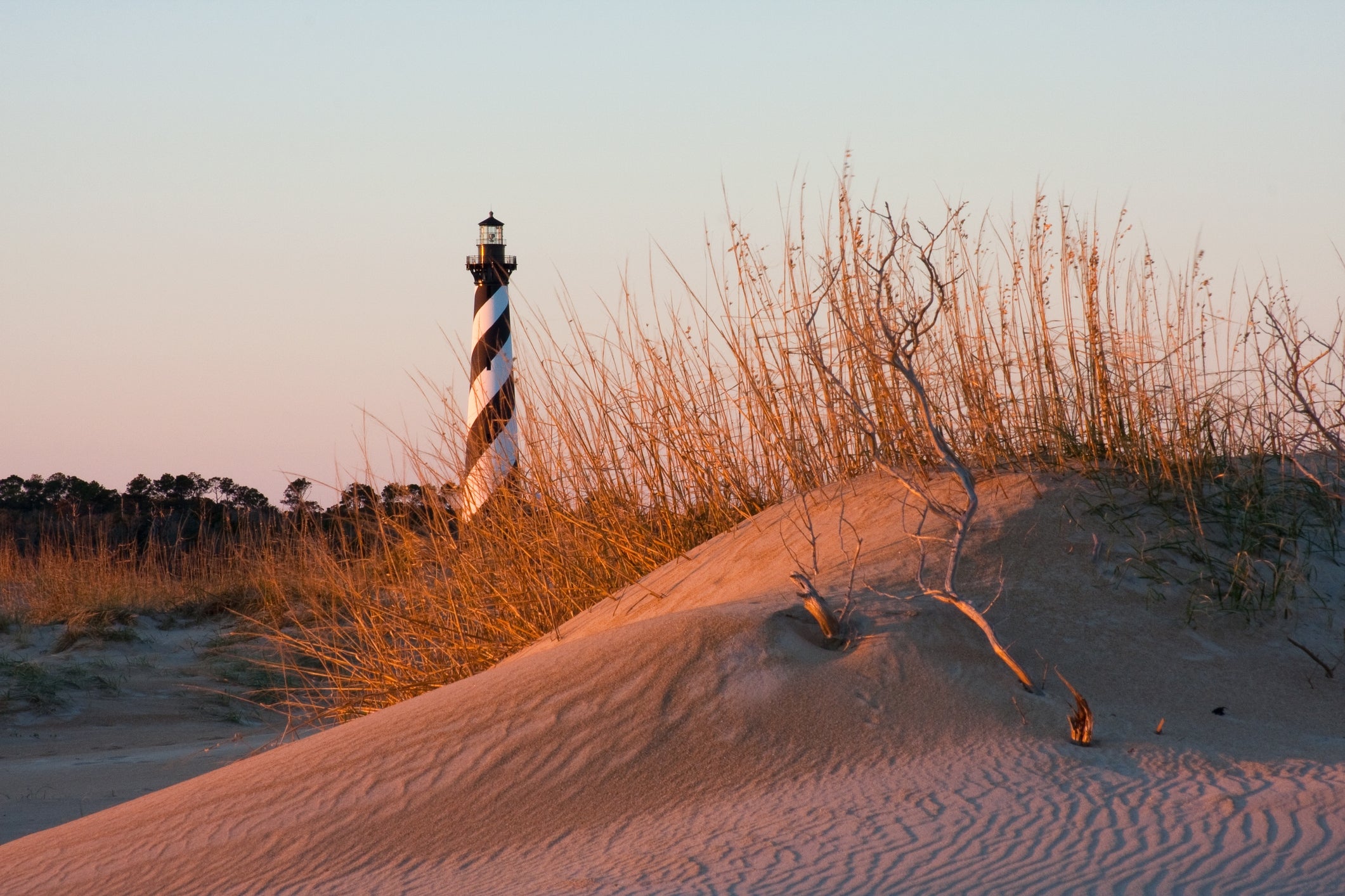 Lighthouse stands down  soil  dunes and adust  grass, with a wide   sky