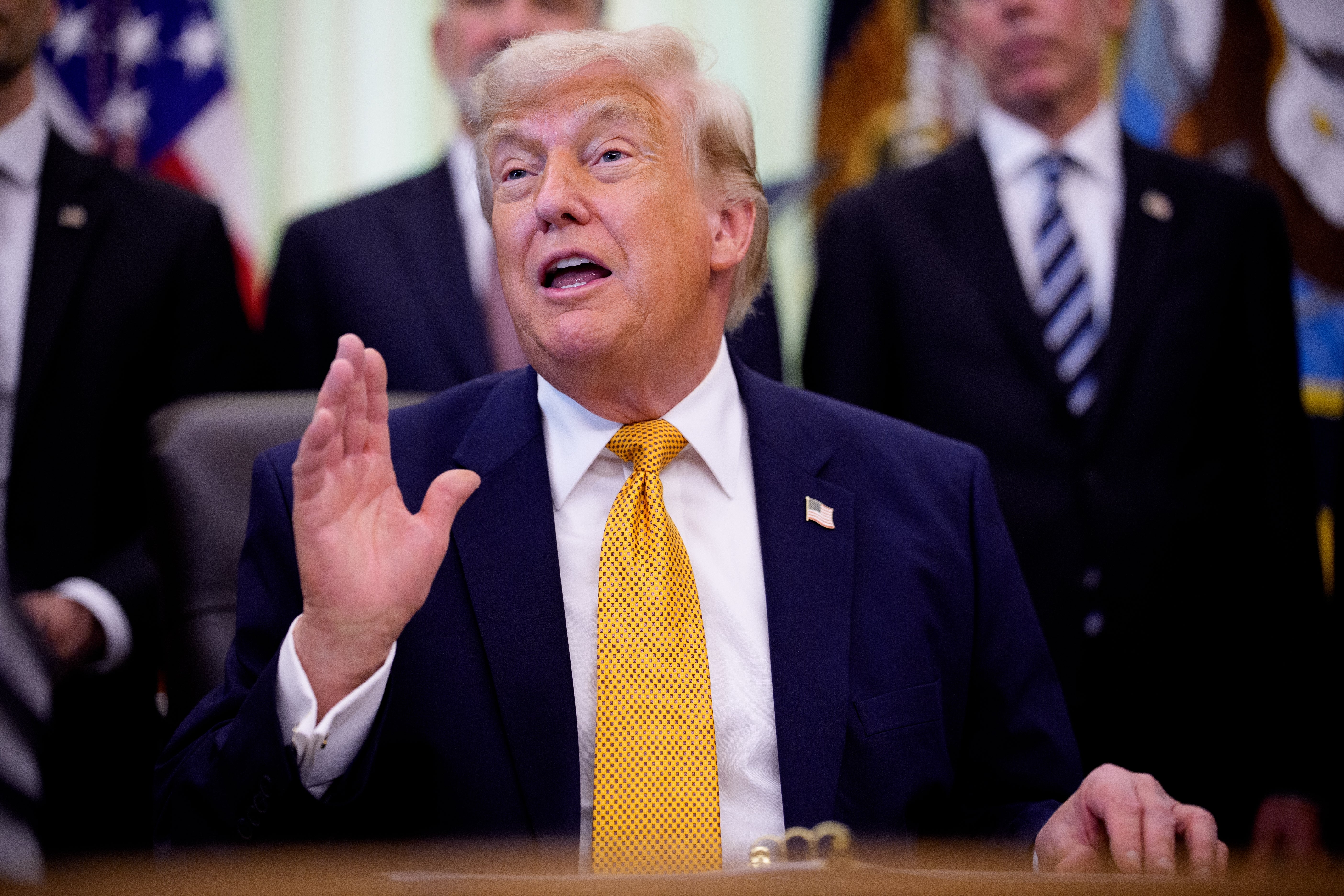 A antheral successful a suit with a yellowish necktie speaks animatedly, gesturing with 1 hand, portion radical basal successful the background