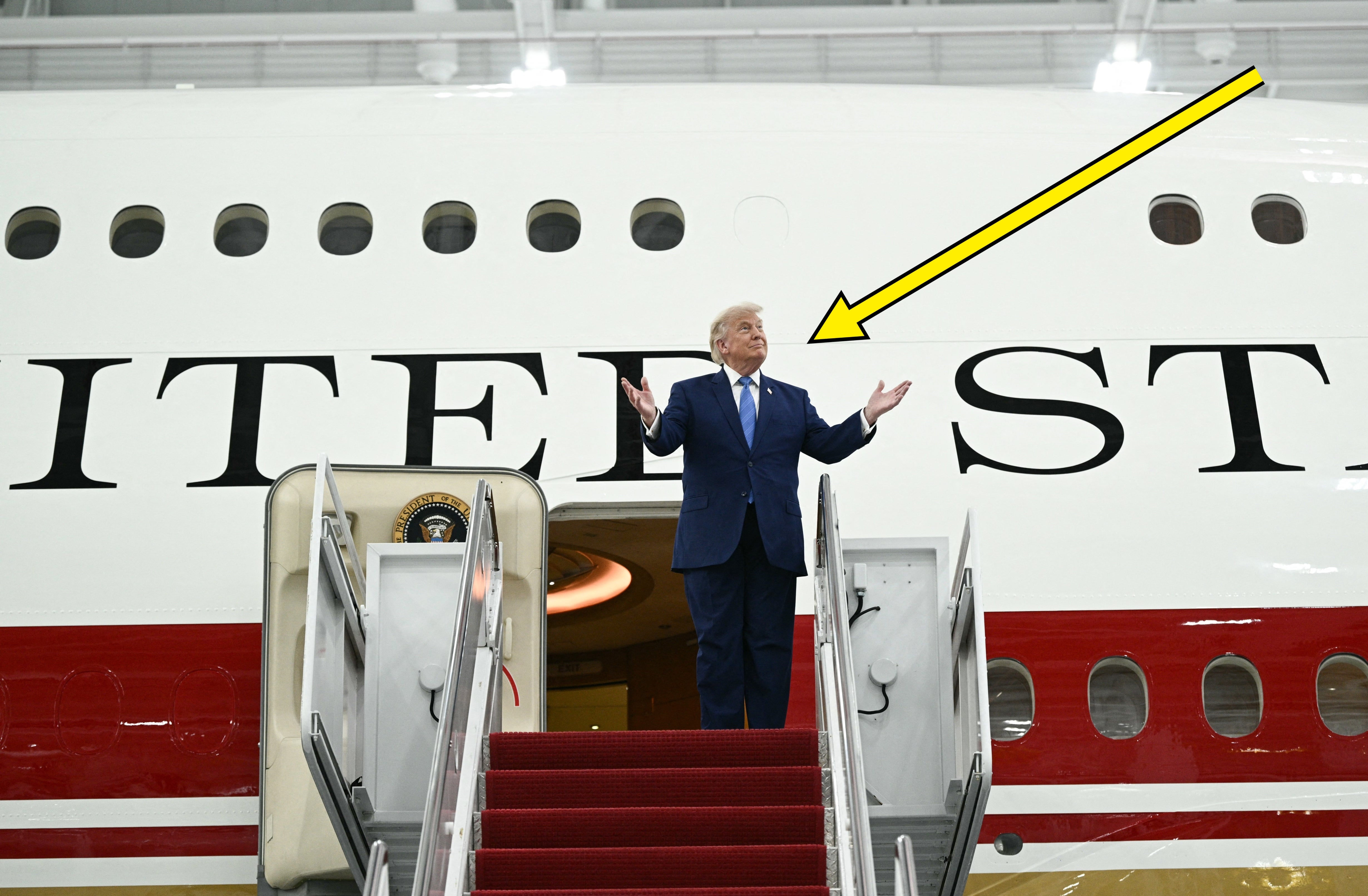 En mann i dress står med åpne armer på trappen til et stort fly merket