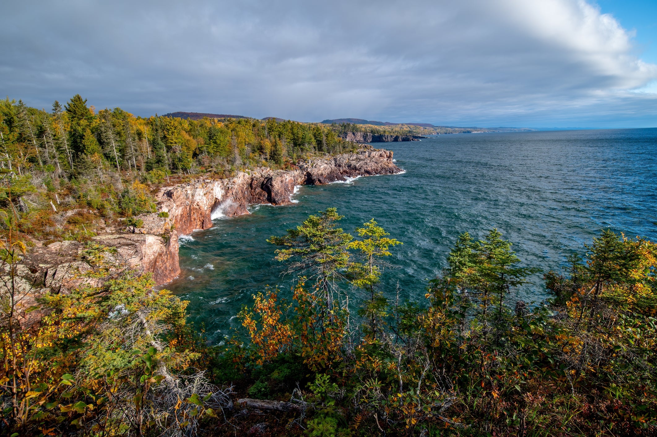 Scenic presumption    of a rocky coastline with trees and a immense   assemblage  of h2o  nether  a cloudy sky