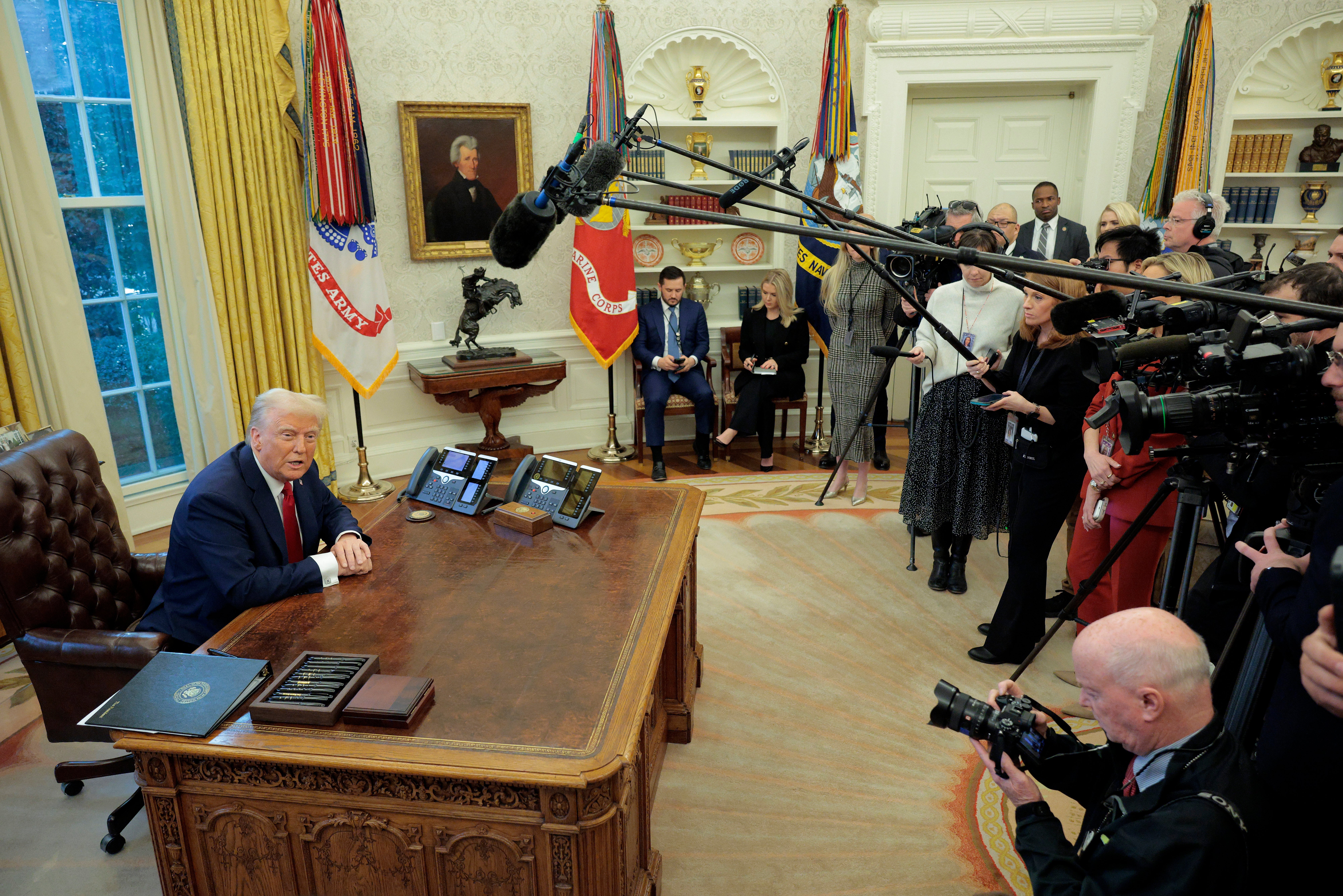 A idiosyncratic sits astatine a table successful an oval office, surrounded by media unit with cameras and microphones