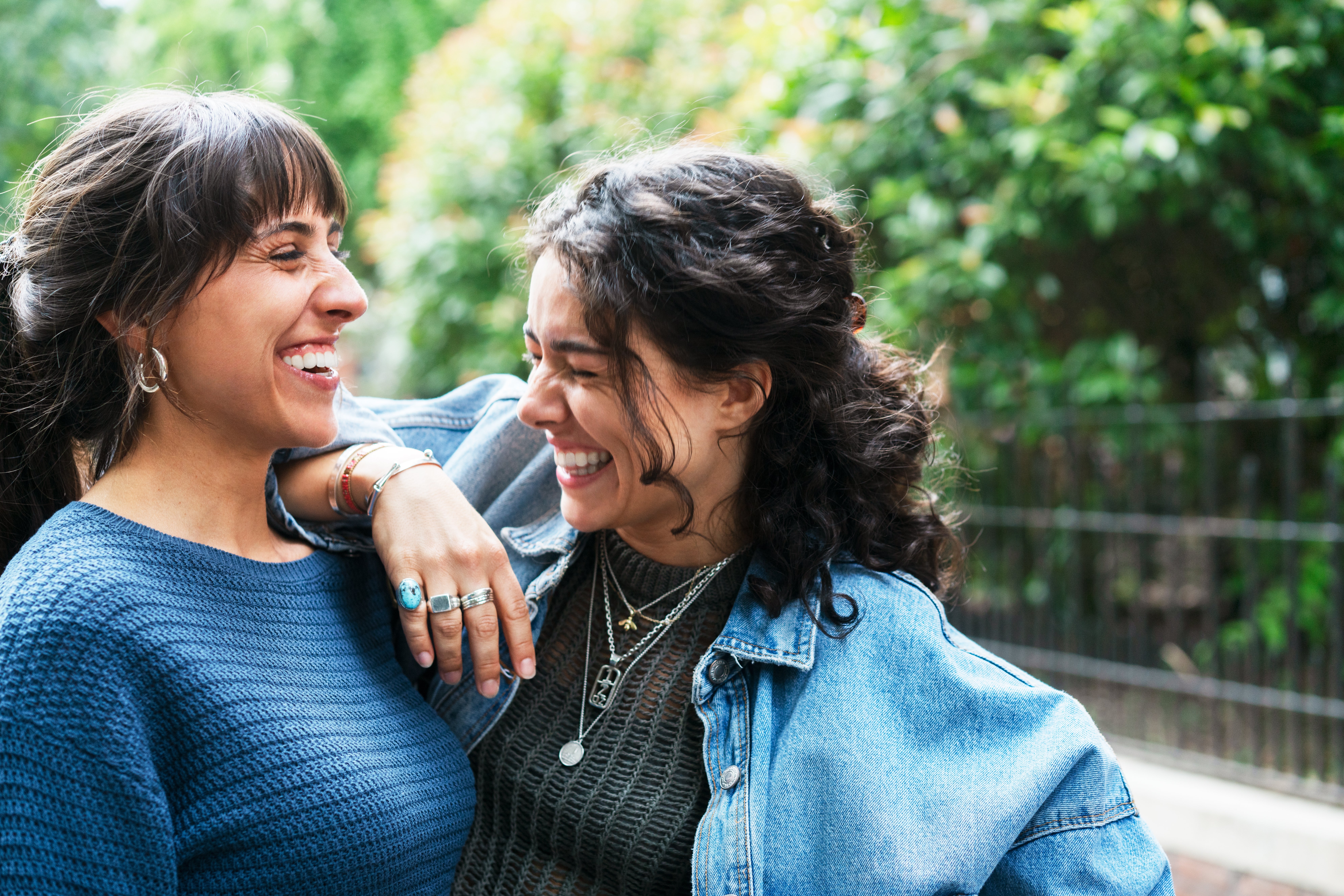 Two radical   laughing unneurotic  outdoors, 1  successful  a bluish  sweater and the different   successful  a denim jacket, showing a joyful moment