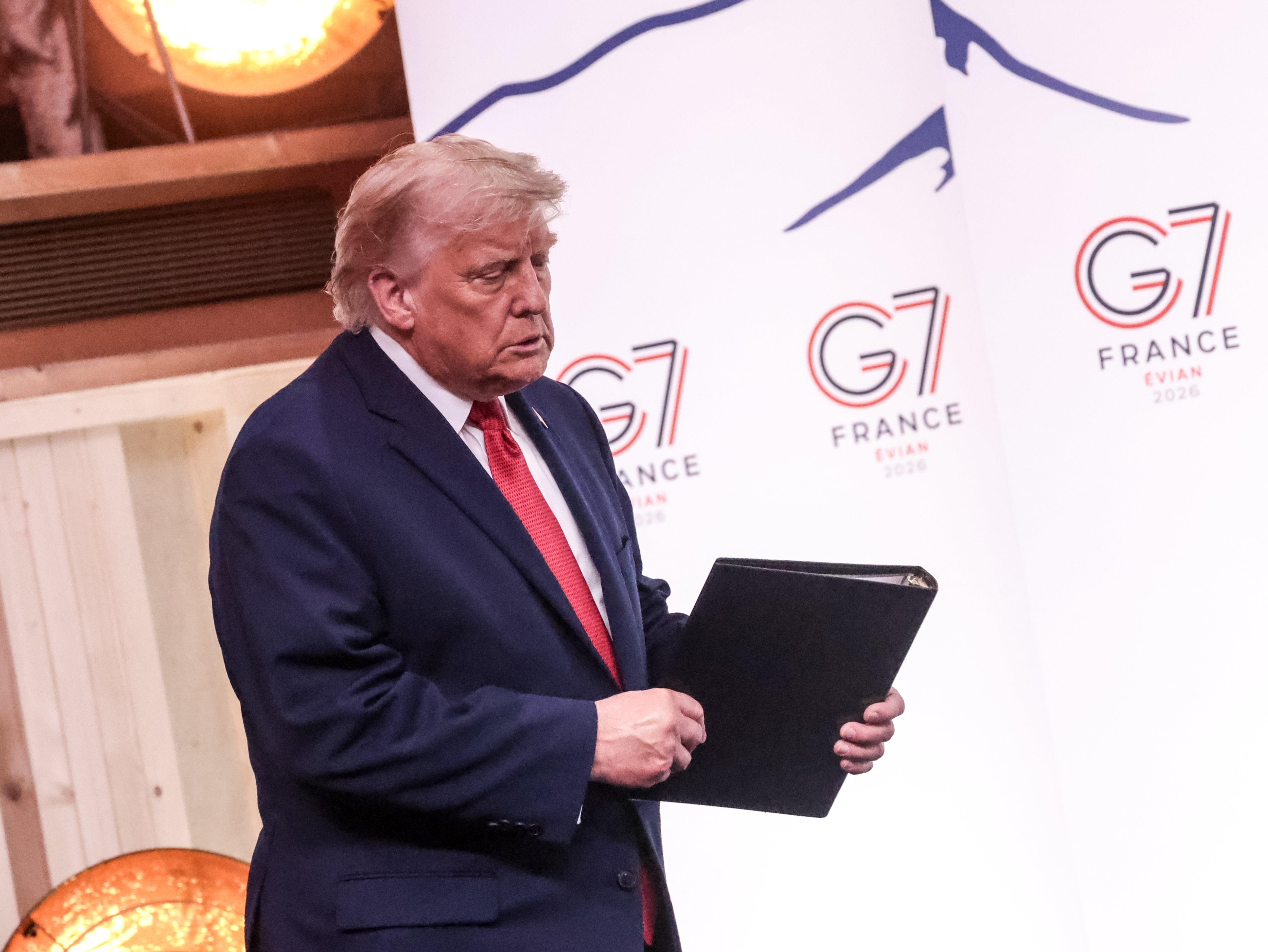 En person i dress som holder en mappe, står ved et G7-toppmøte i Frankrike