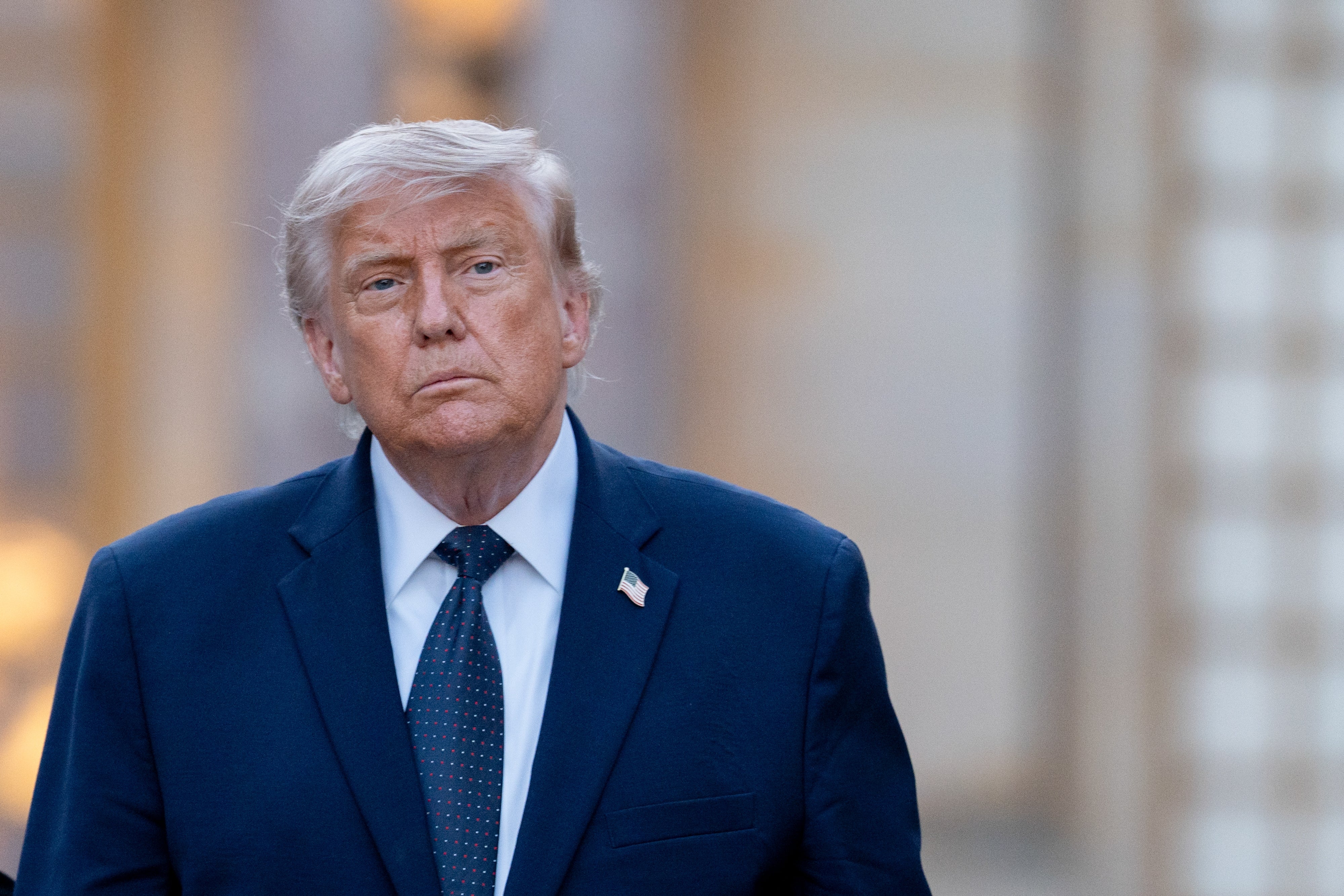 A idiosyncratic   successful  a suit   with an American emblem  pin walks outside, looking serious. Background suggests an municipality  setting