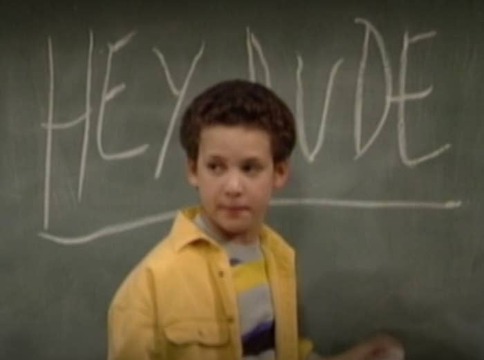 Young idiosyncratic   successful  a schoolroom  stands successful  beforehand   of a chalkboard with "HEY DUDE" written connected  it