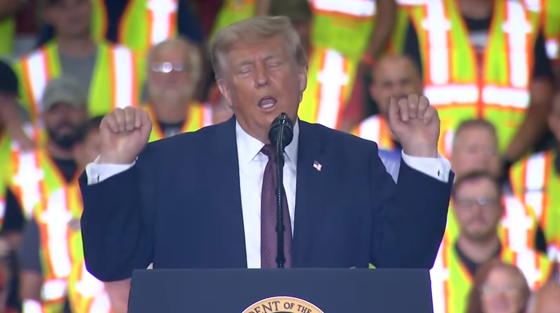A idiosyncratic   successful  a suit   speaks astatine  a podium, gesturing upwards. Audience members successful  information   vests are successful  the background