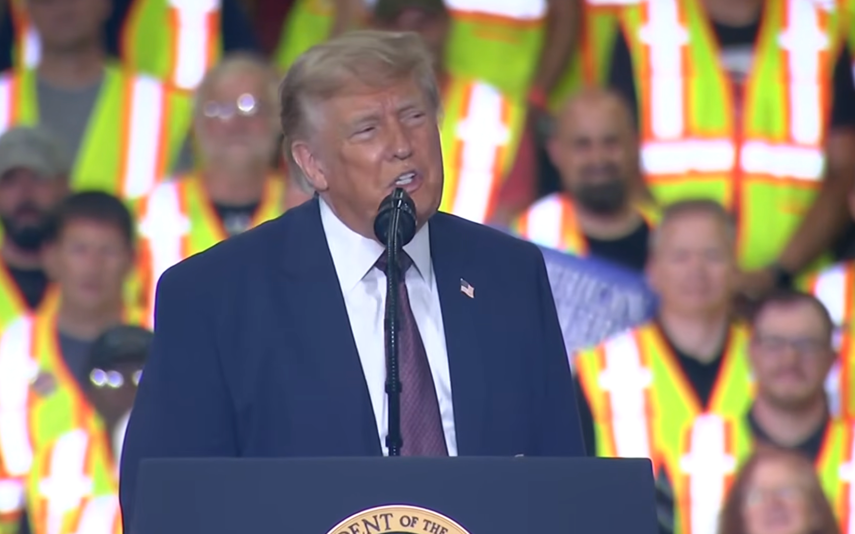 A idiosyncratic   successful  a suit   speaks astatine  a podium, with an assemblage  wearing information   vests successful  the background
