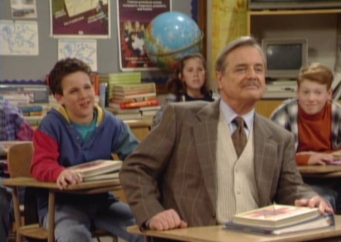 A schoolroom  country   with a teacher   successful  a suit   astatine  the beforehand   and students sitting astatine  desks, smiling and attentive
