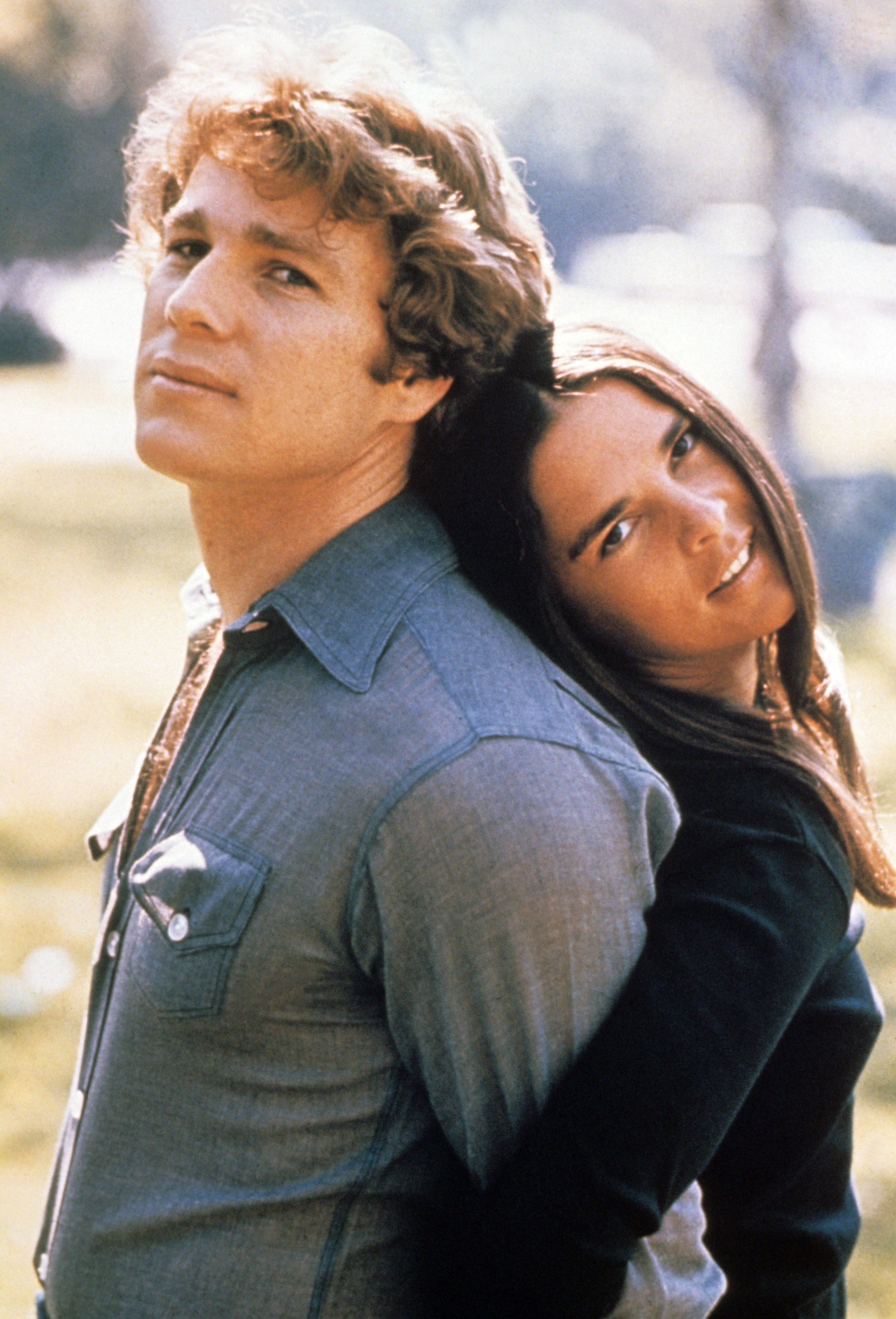 A mates  poses intimately  outdoors, with the pistillate   leaning her caput  connected  the man's shoulder. Both are stylishly dressed