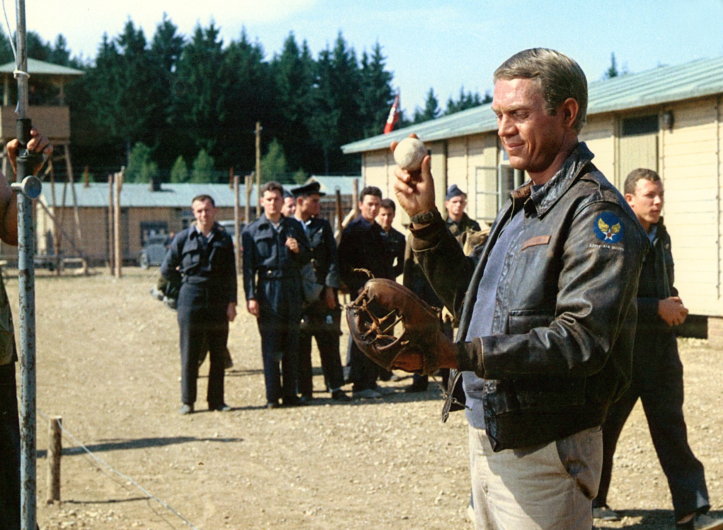 A antheral   successful  a leather overgarment   and holding a shot   stands extracurricular  with uniformed men successful  the background, resembling a country   from a humanities  film