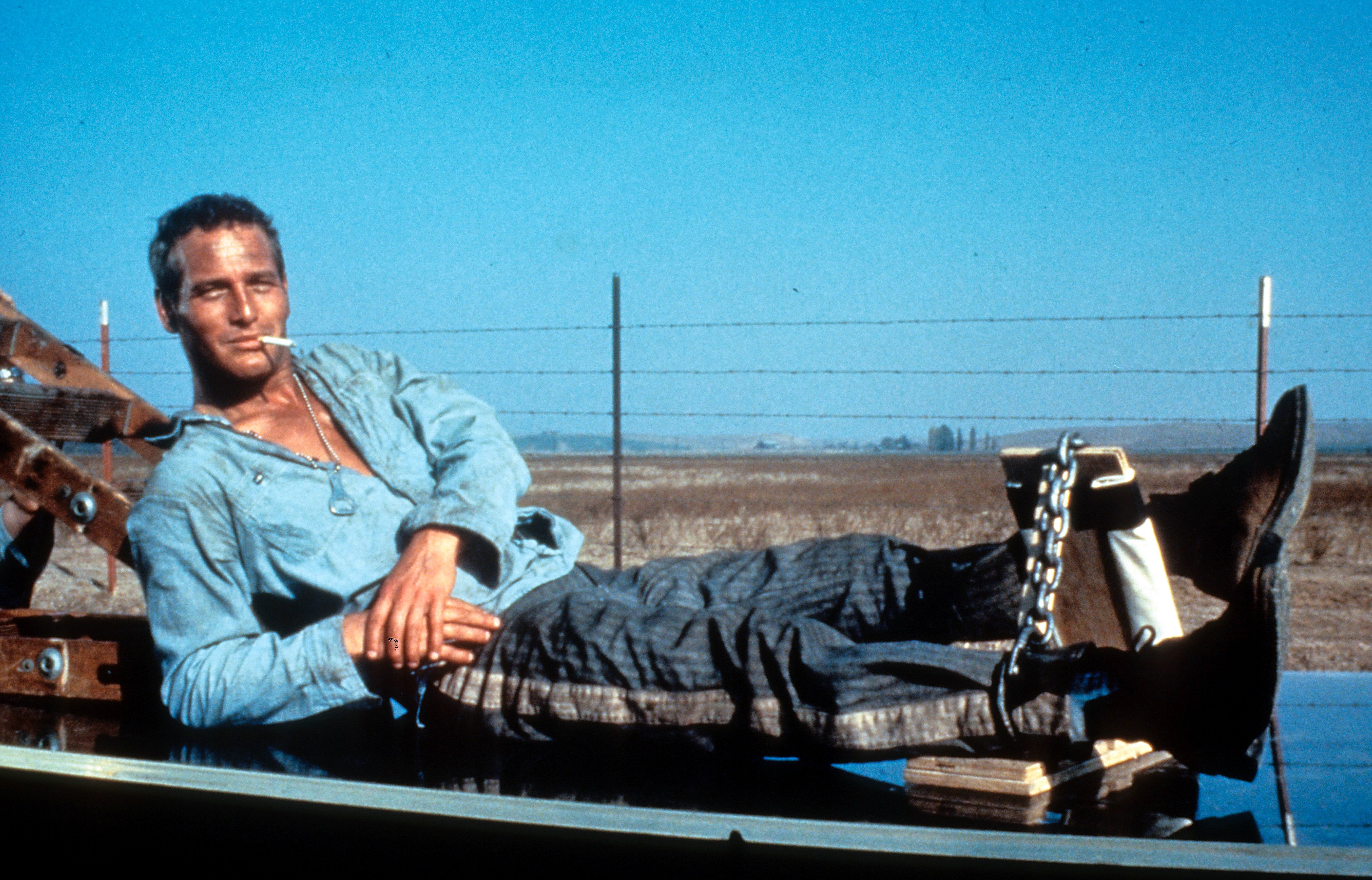 Person reclining casually outdoors, wearing a denim garment  and striped pants, with a concatenation  connected  1  leg, mounting  a relaxed, rebellious tone