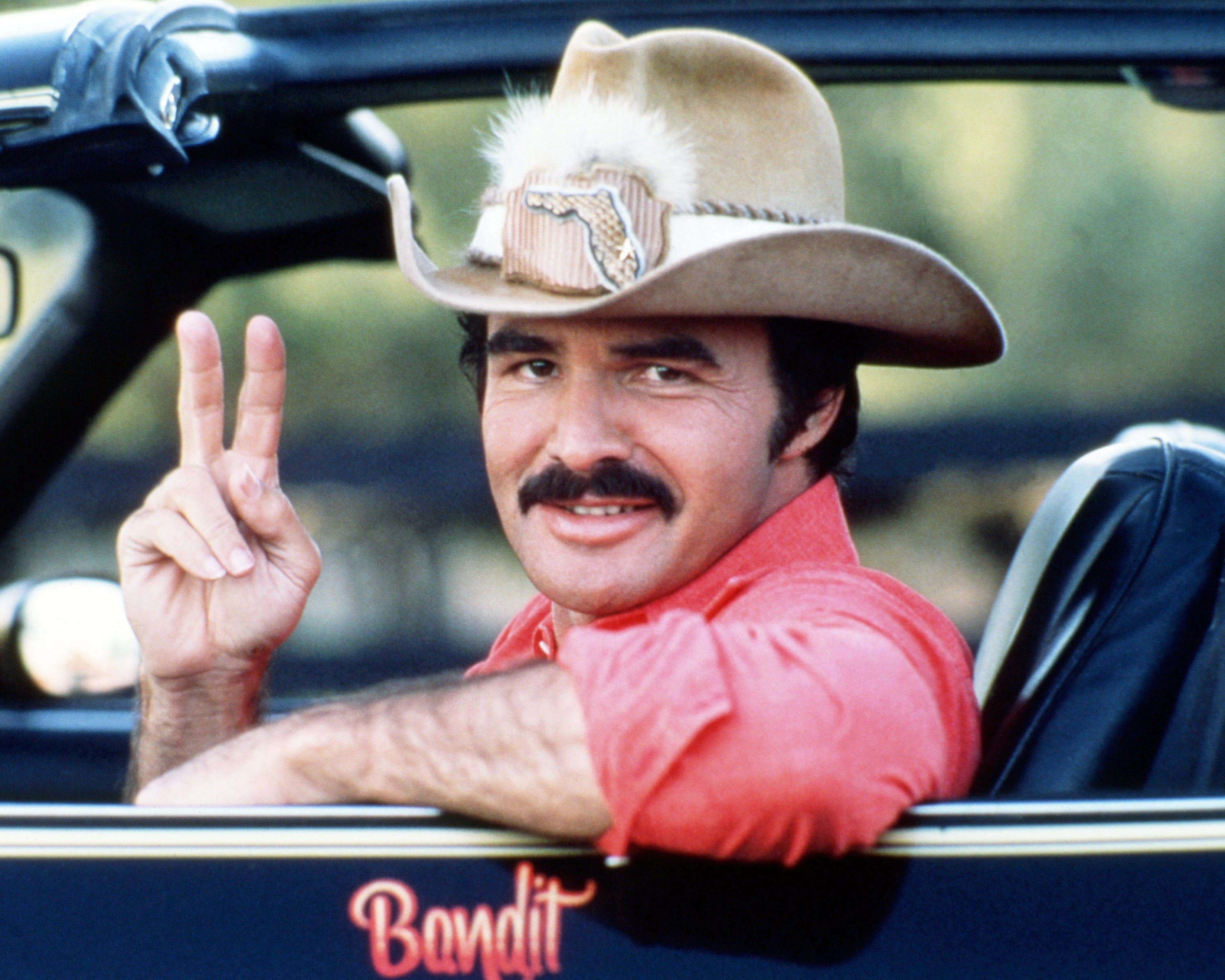 Actor successful  cowboy chapeau  flashes bid    motion   from a car   window; known for a charming grin  and rugged style