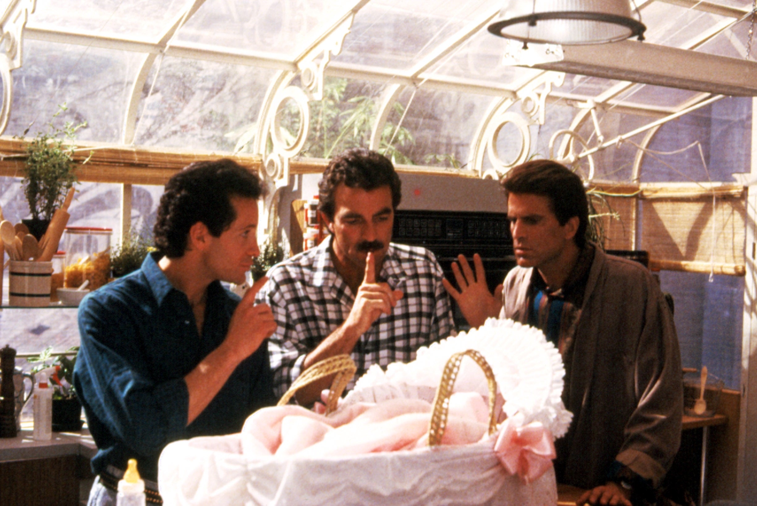 Three men successful  casual 80s attire basal   astir   a babe  successful  a bassinet, gesturing to beryllium  quiet, suggesting a comedic scene