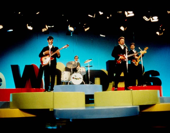 Band performing connected  a colorful signifier    with large, bold letters successful  the background. Members play   guitar, drums, and bass. Vibrant, energetic scene
