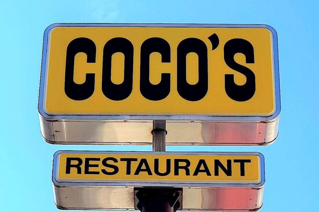 「COCO'S」と書かれたレストランの看板が空を背景に掲げられている。