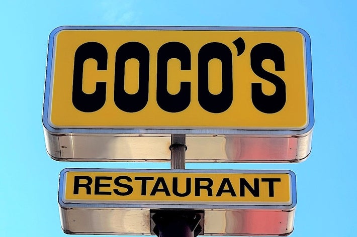 「COCO'S」と書かれたレストランの看板が空を背景に掲げられている。