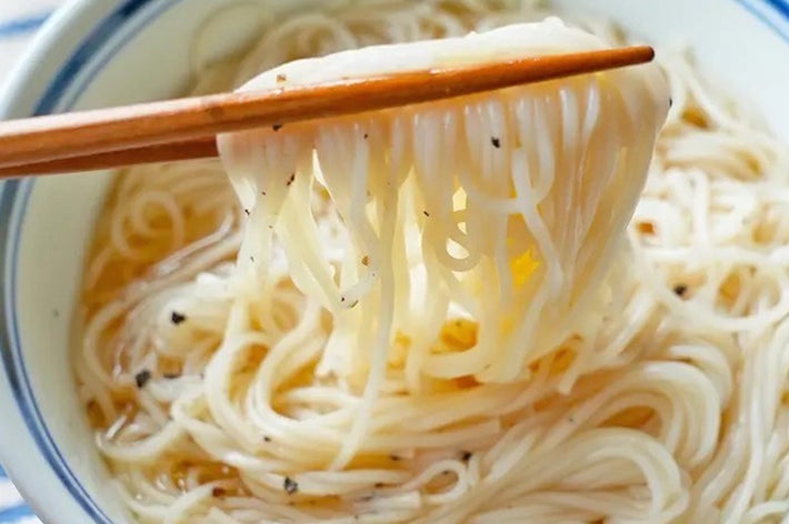箸で掴んだそうめんのアップ。器にはスープが少量あり、シンプルな食事の一例を示しています。