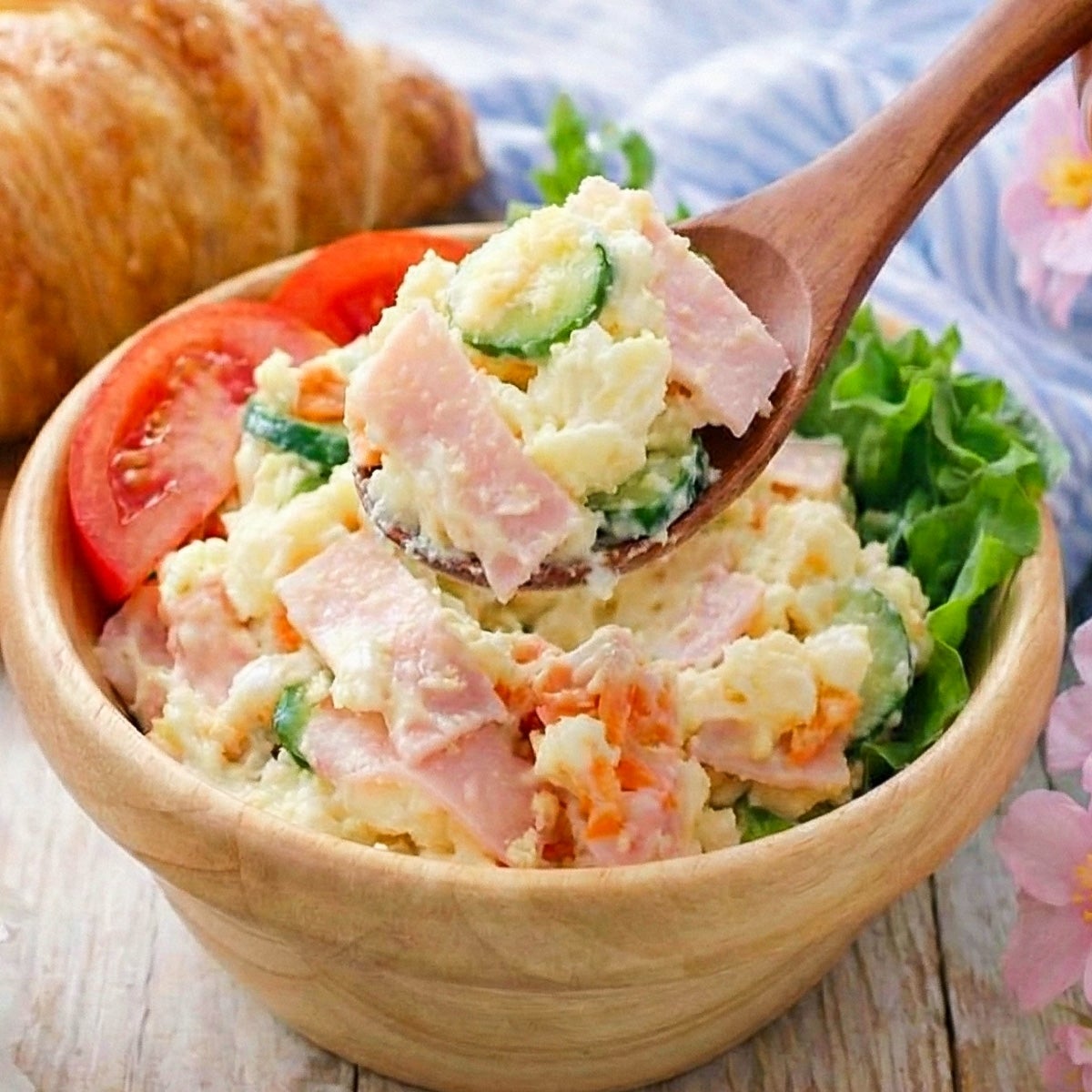 じゃがいもサラダに、ハム、きゅうり、にんじんが入った一皿。トマトとクロワッサンが添えられている。