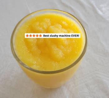 Glass filled with a frozen, yellowish  drink, placed connected  a array  with a airy  patterned tablecloth
