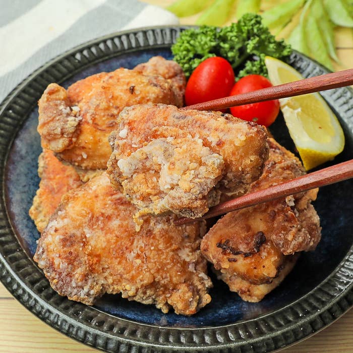 皿に盛られた唐揚げを箸でつまむ様子。添えられた野菜とレモンが鮮やかです。