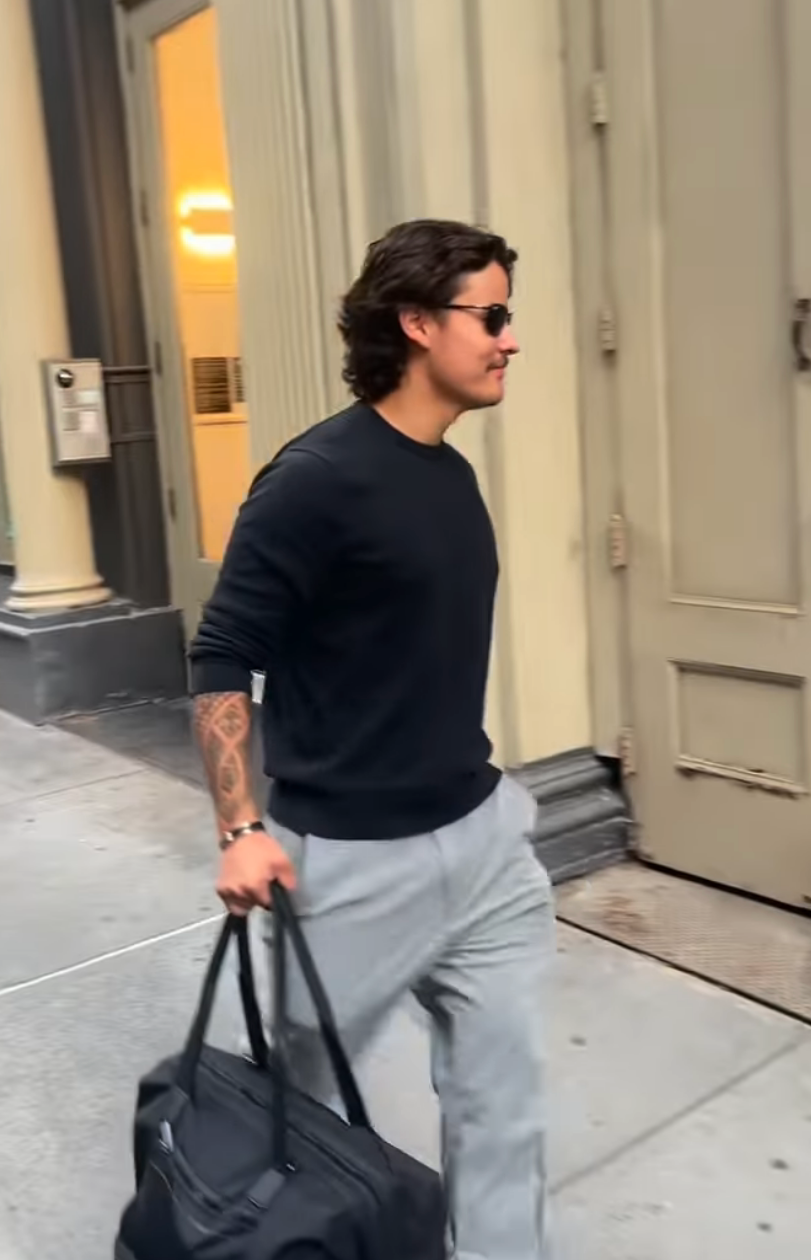 Collin successful  casual attire holding a bag, walking connected  a metropolis  sidewalk with a disposable   tattoo connected  their forearm