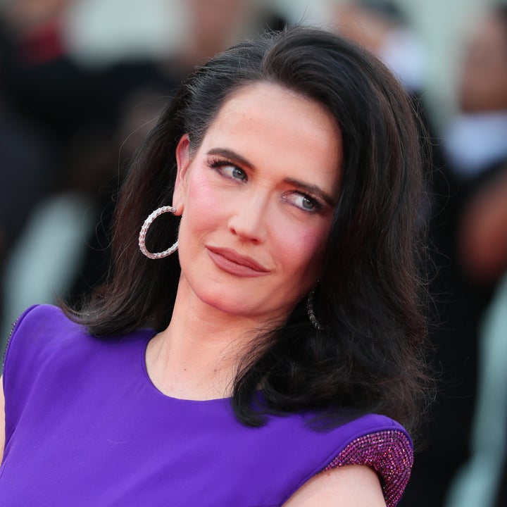 A person poses on the red carpet in an elegant outfit with bold hoop earrings, looking to the side with a confident expression