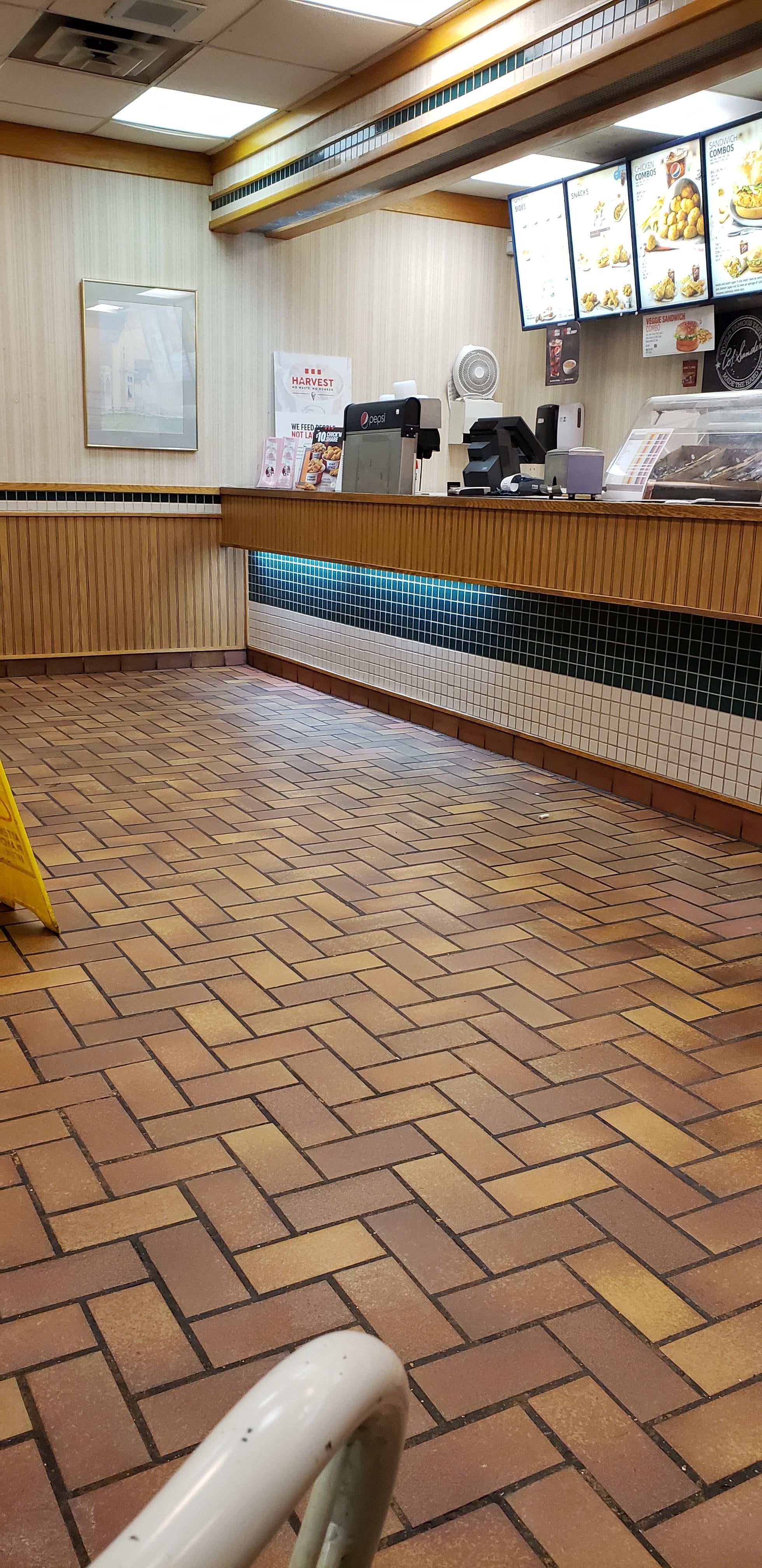 Empty fast-food restaurant counter with a menu board above. No customers or staff visible