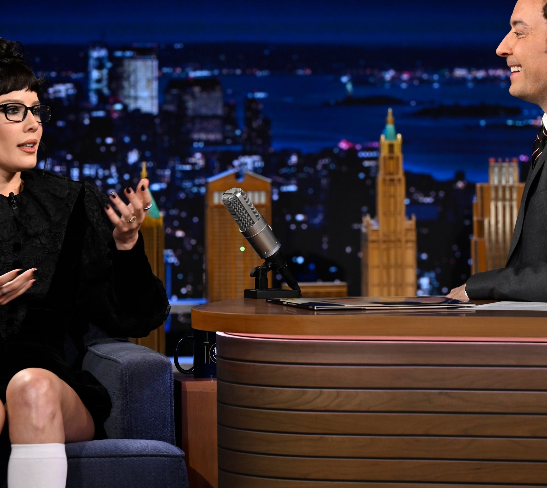 Halsey sitting down on a talk show in a stylish outfit with glasses and tall socks