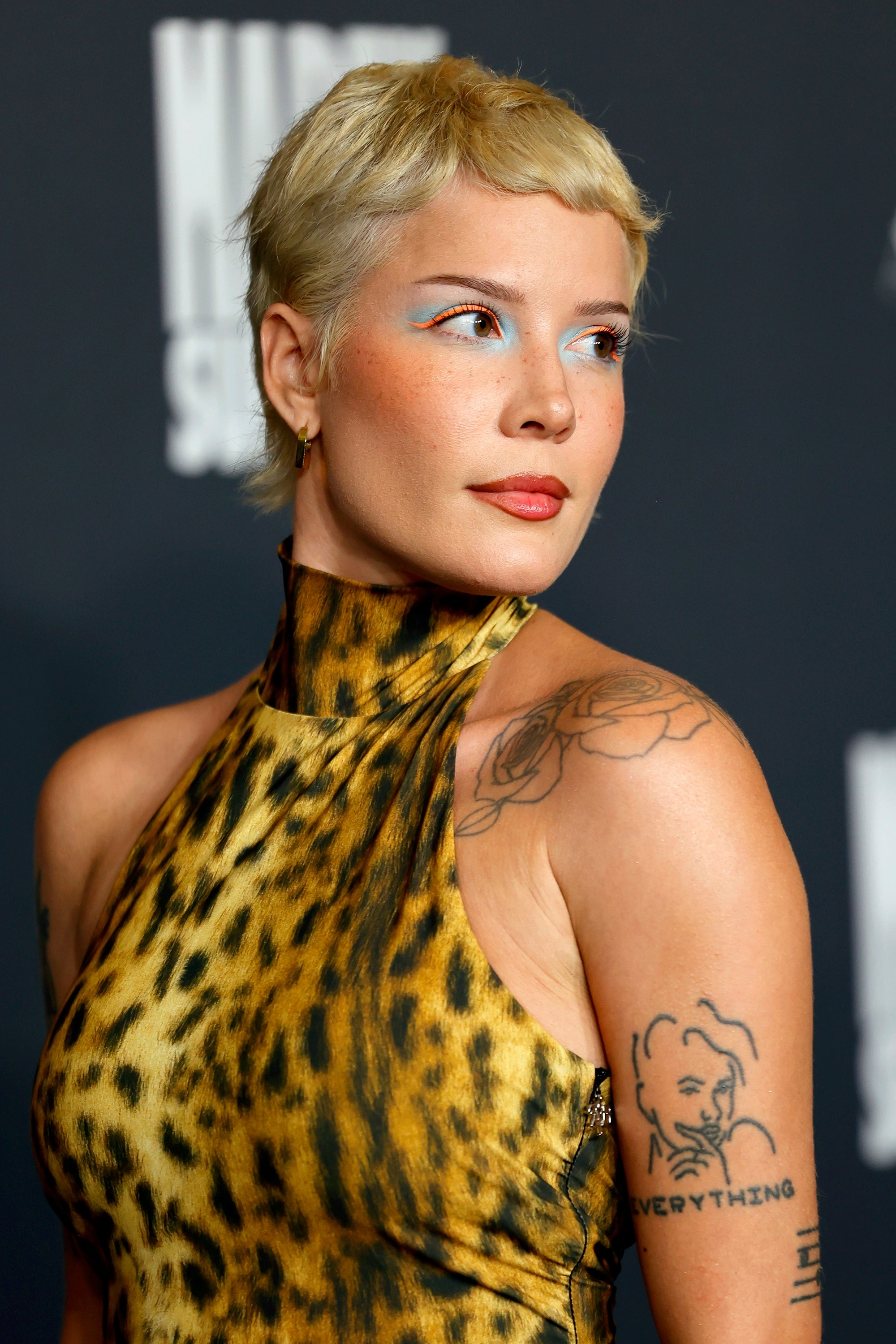 Halsey poses on the red carpet in a leopard-print halter dress with bold makeup and visible tattoos