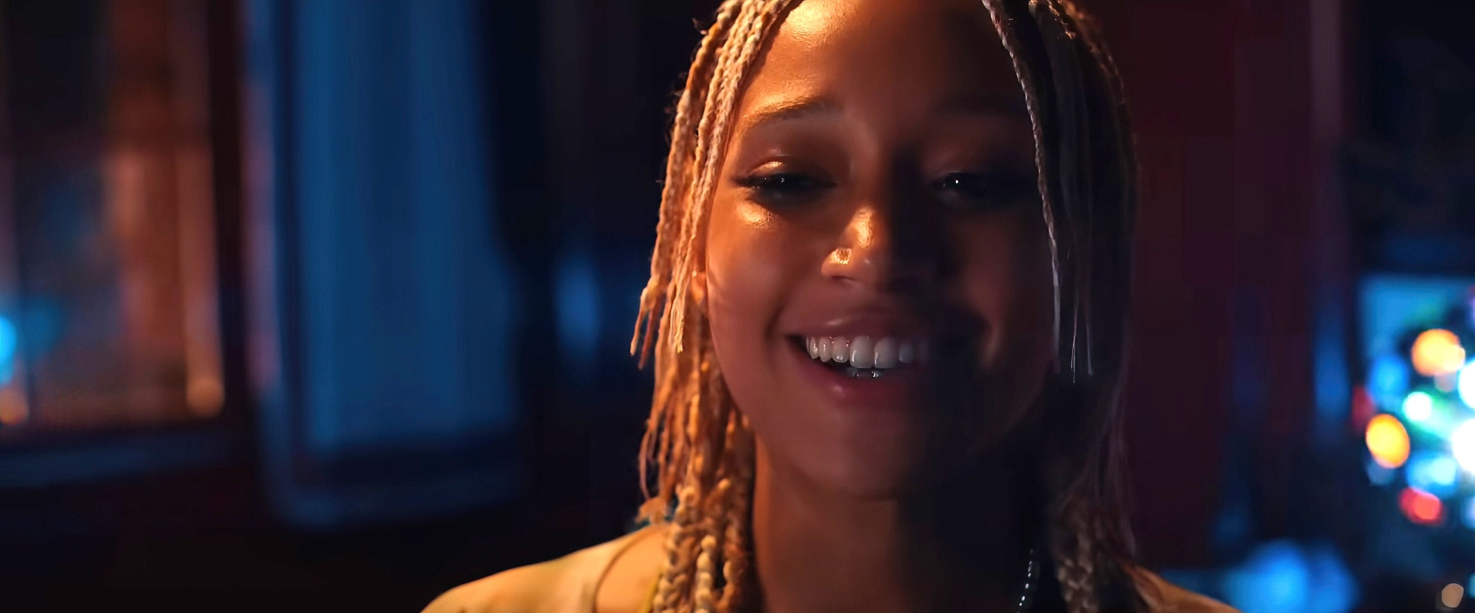 Amandla Stenberg with braided hair smiles warmly, seemingly lit in a media or entertainment setting