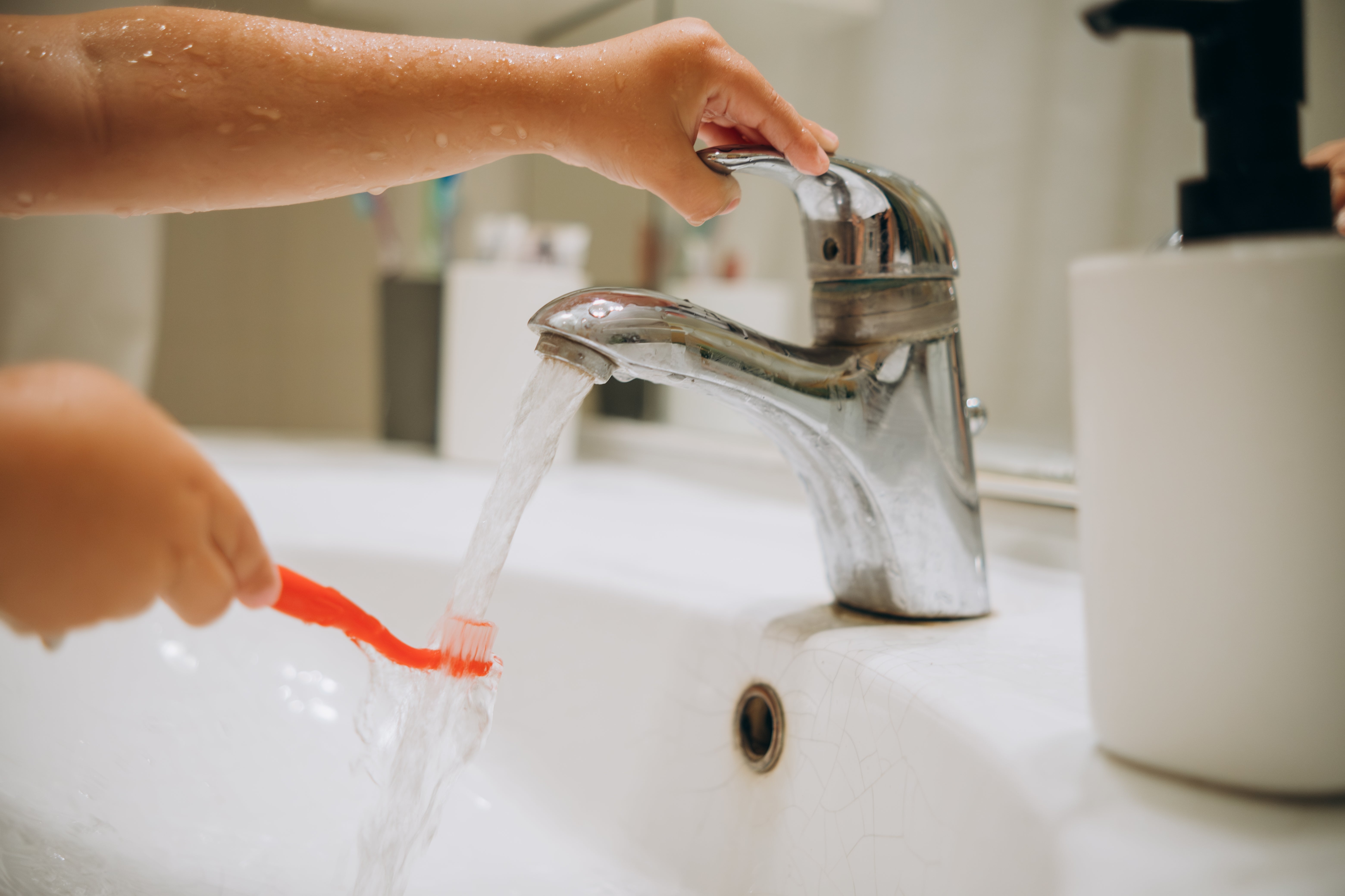 A kid  rinses a toothbrush nether  a moving  faucet, illustrating a regular  hygiene regular    successful  a work-life context