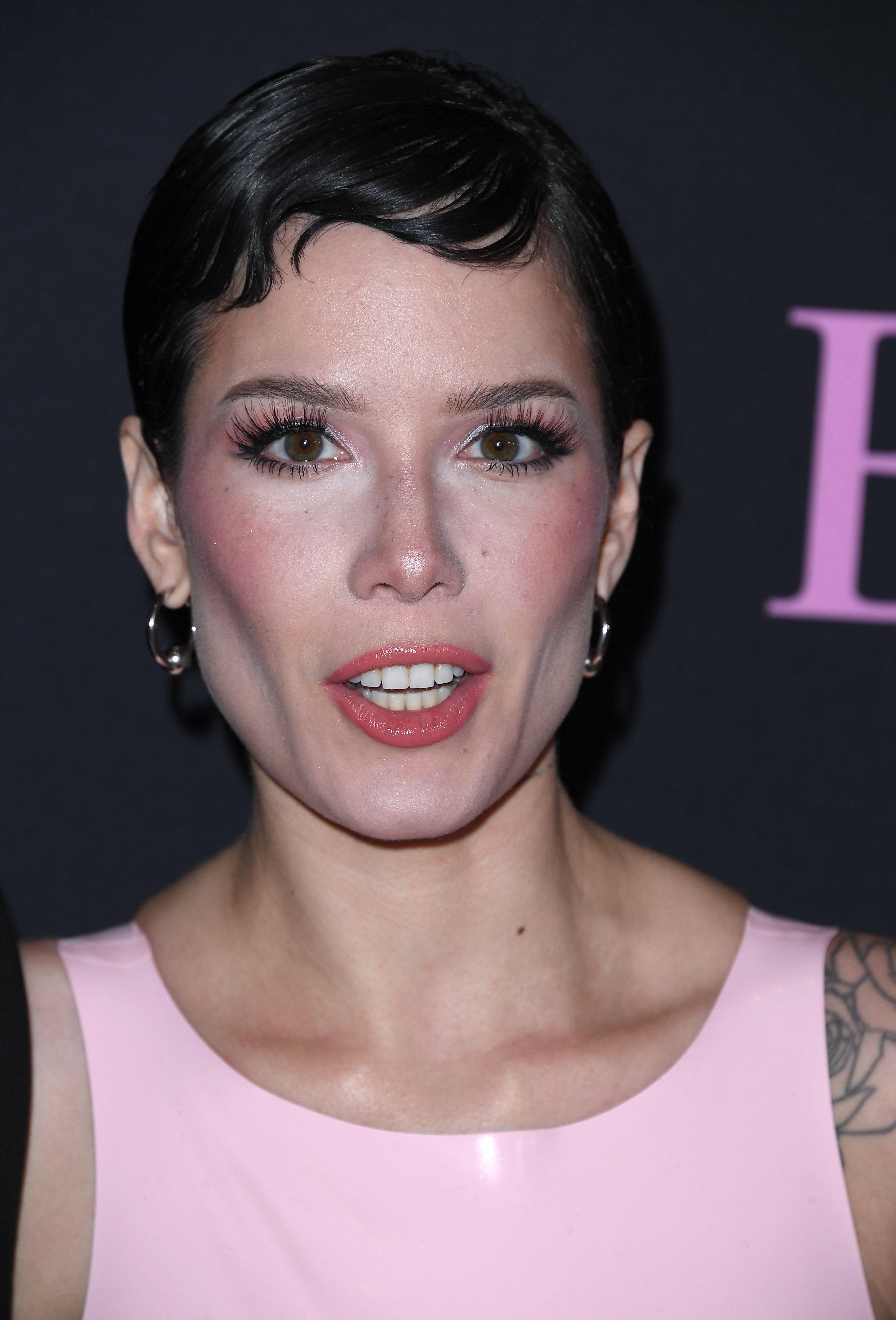 Halsey with short hair and hoop earrings at a celebrity event, wearing a sleeveless outfit