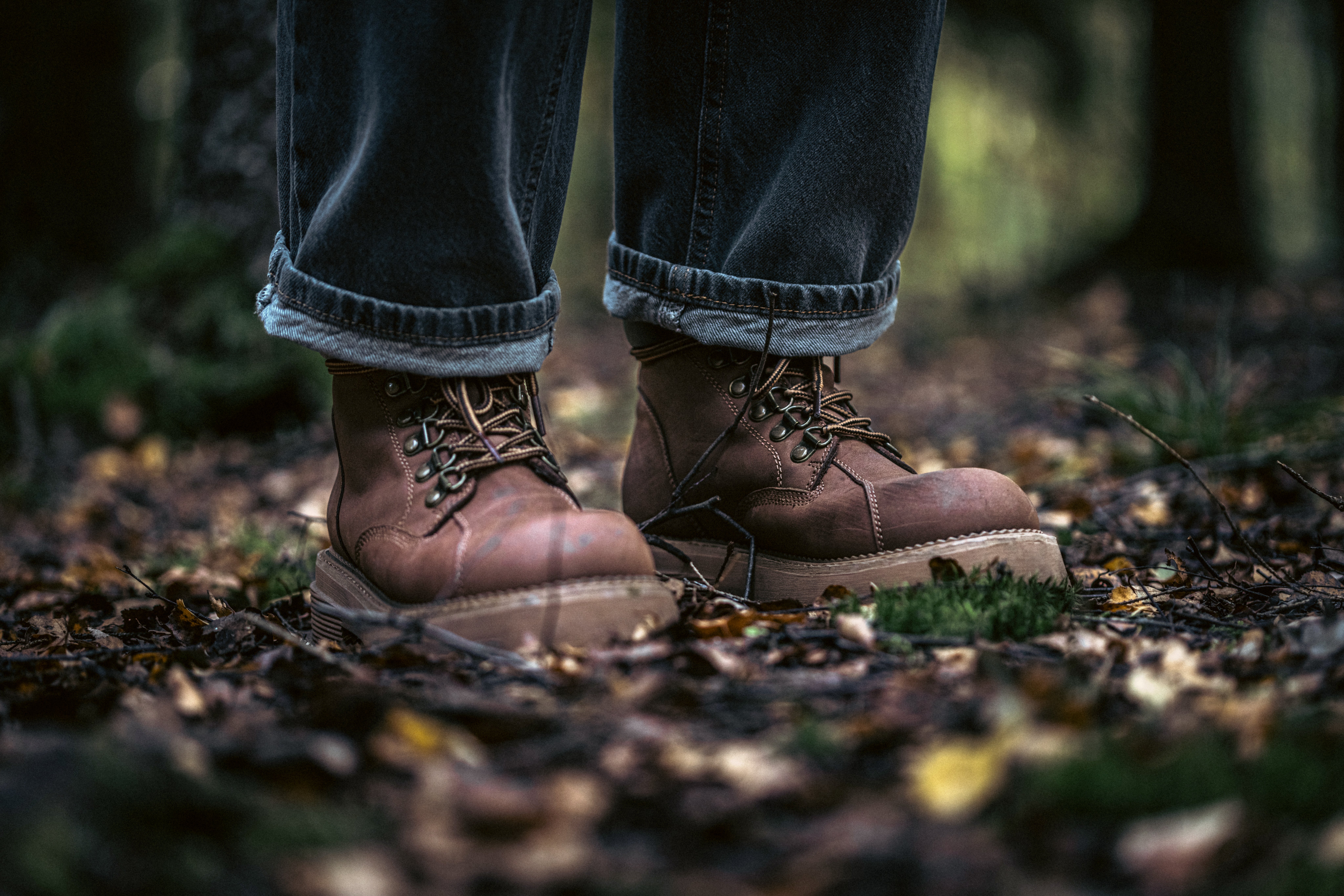 Person successful  rolled-up jeans and rugged enactment    boots stands connected  a leafy wood  floor, emphasizing outdoor enactment    readiness