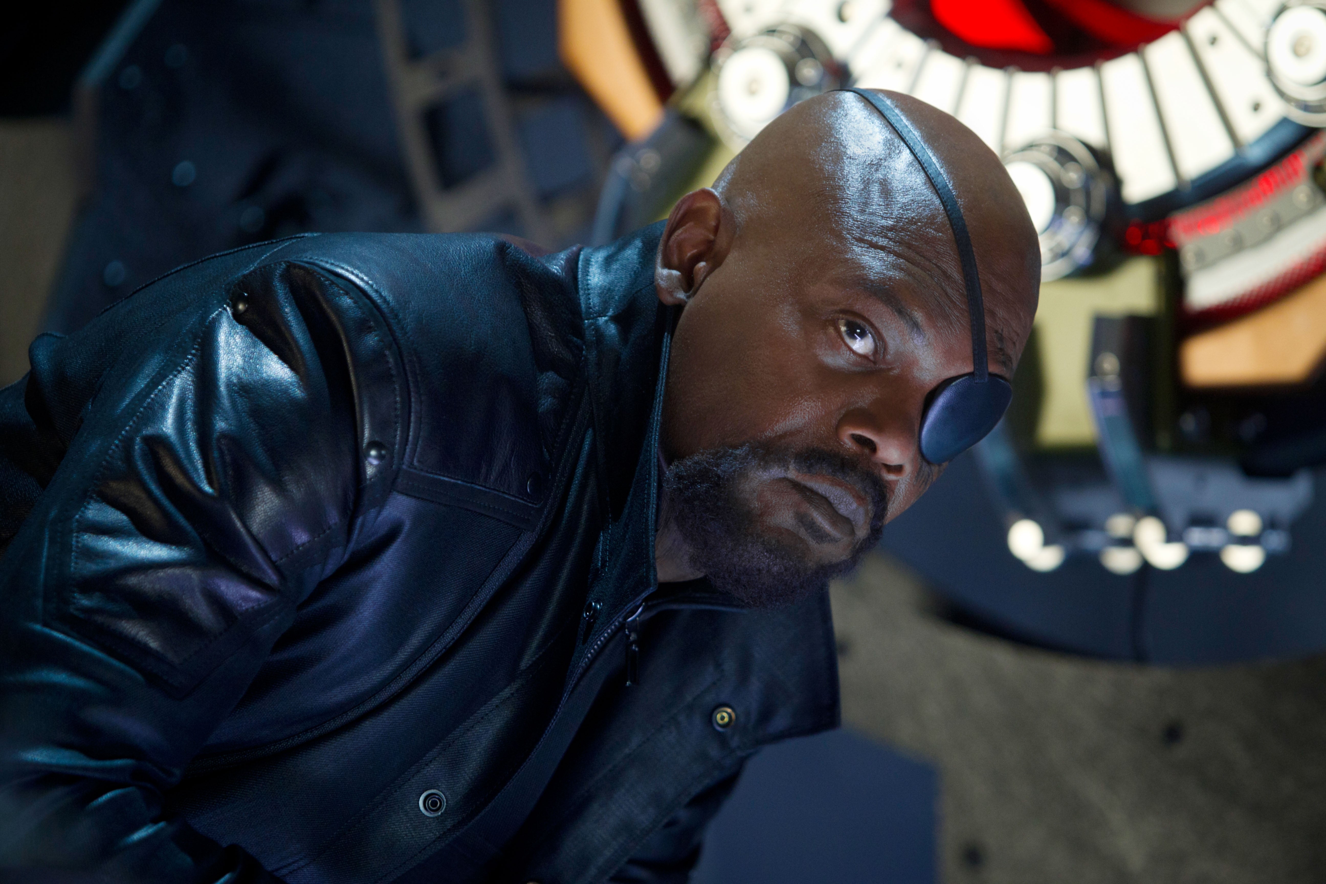 Samuel L Jackson wearing a leather jacket and an eyepatch looks intensely at something in the distance