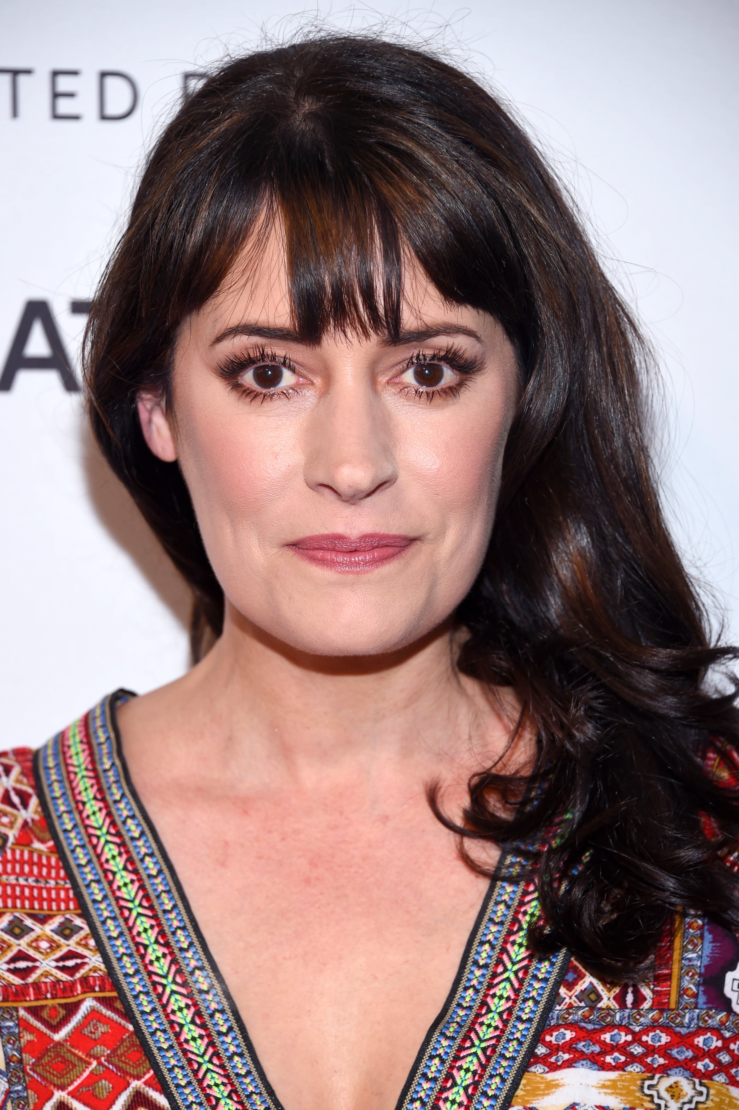 Paget Brewster with long, dark hair wearing a patterned V-neck top at a celebrity event