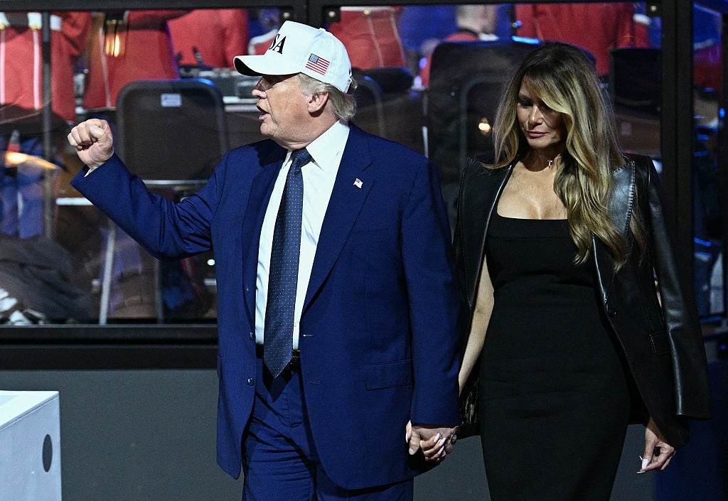 En mann i dress og baseballcap går hånd i hånd med en kvinne i svart kjole og skinnjakke på et arrangement