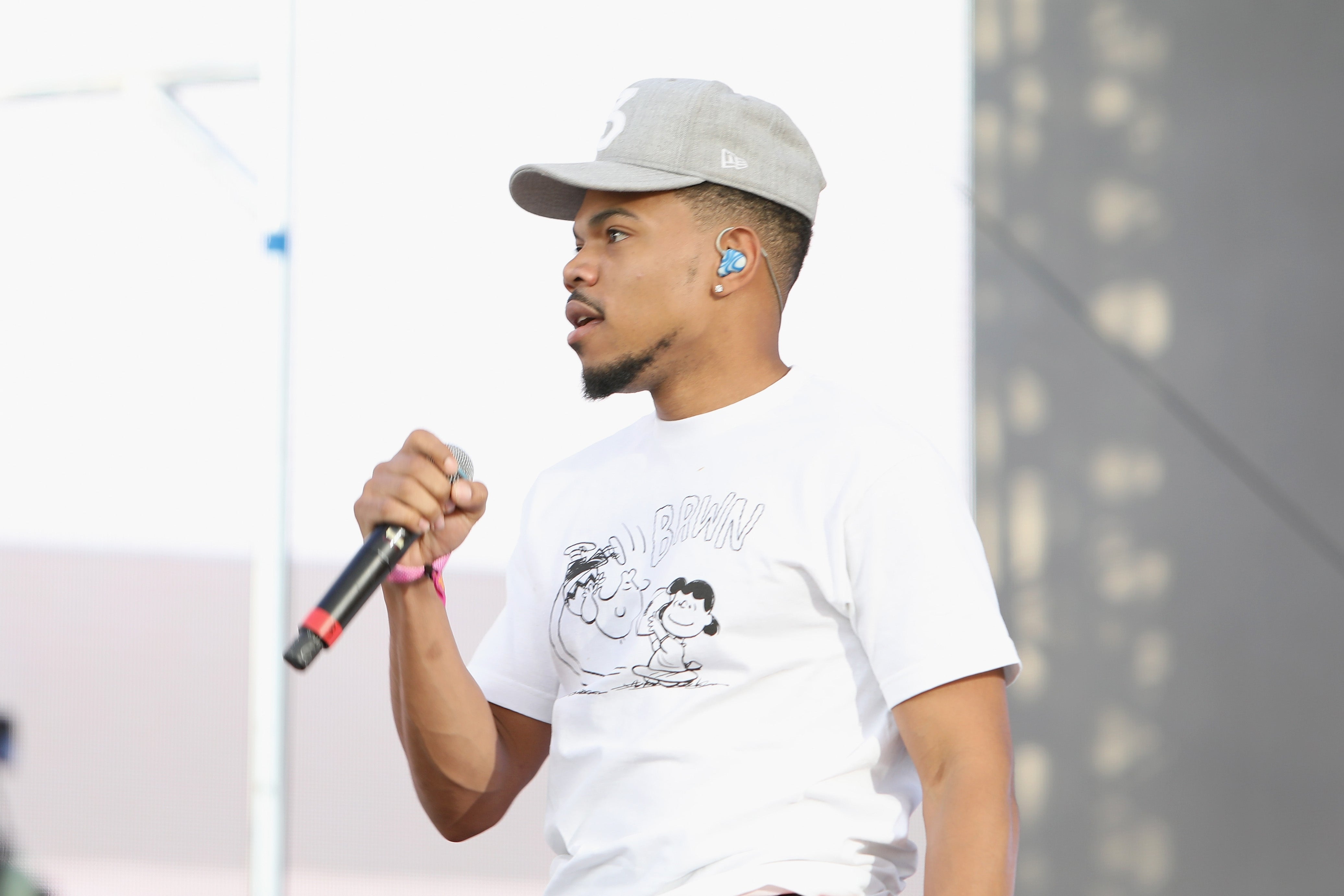 Chance the Rapper in a graphic tee and cap holding a microphone on stage during a performance