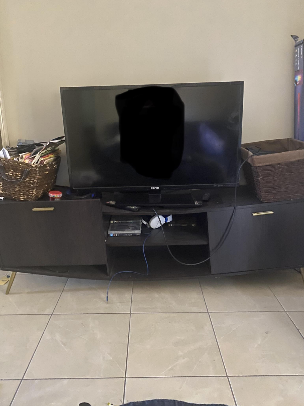 Television on a dark media console with items in baskets on each side, and cables underneath
