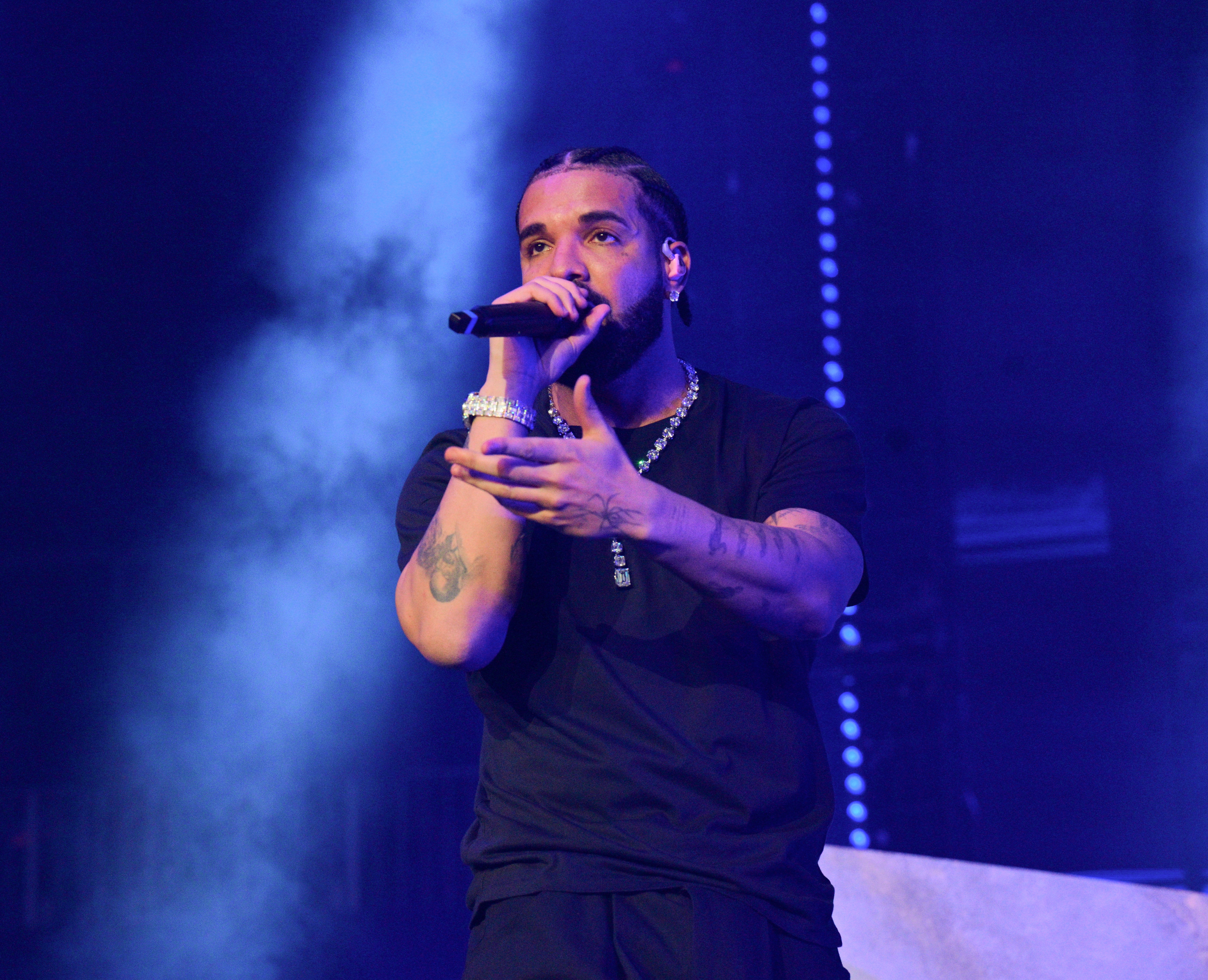Drake performing on stage, wearing a casual outfit with a microphone in hand under dramatic lighting effects