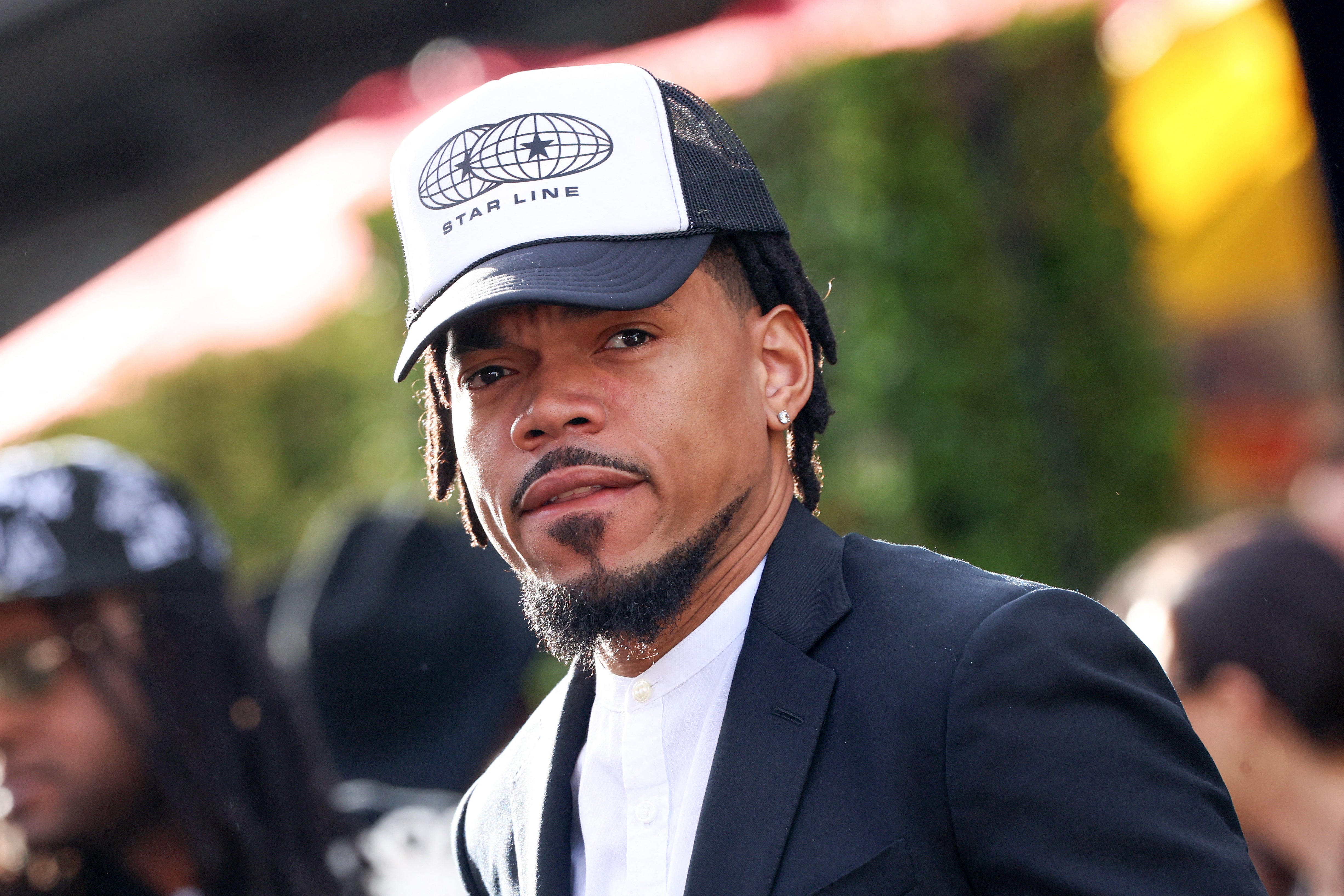 Chance the Rapper in a suit and trucker hat with "Star Line" logo, attending an event