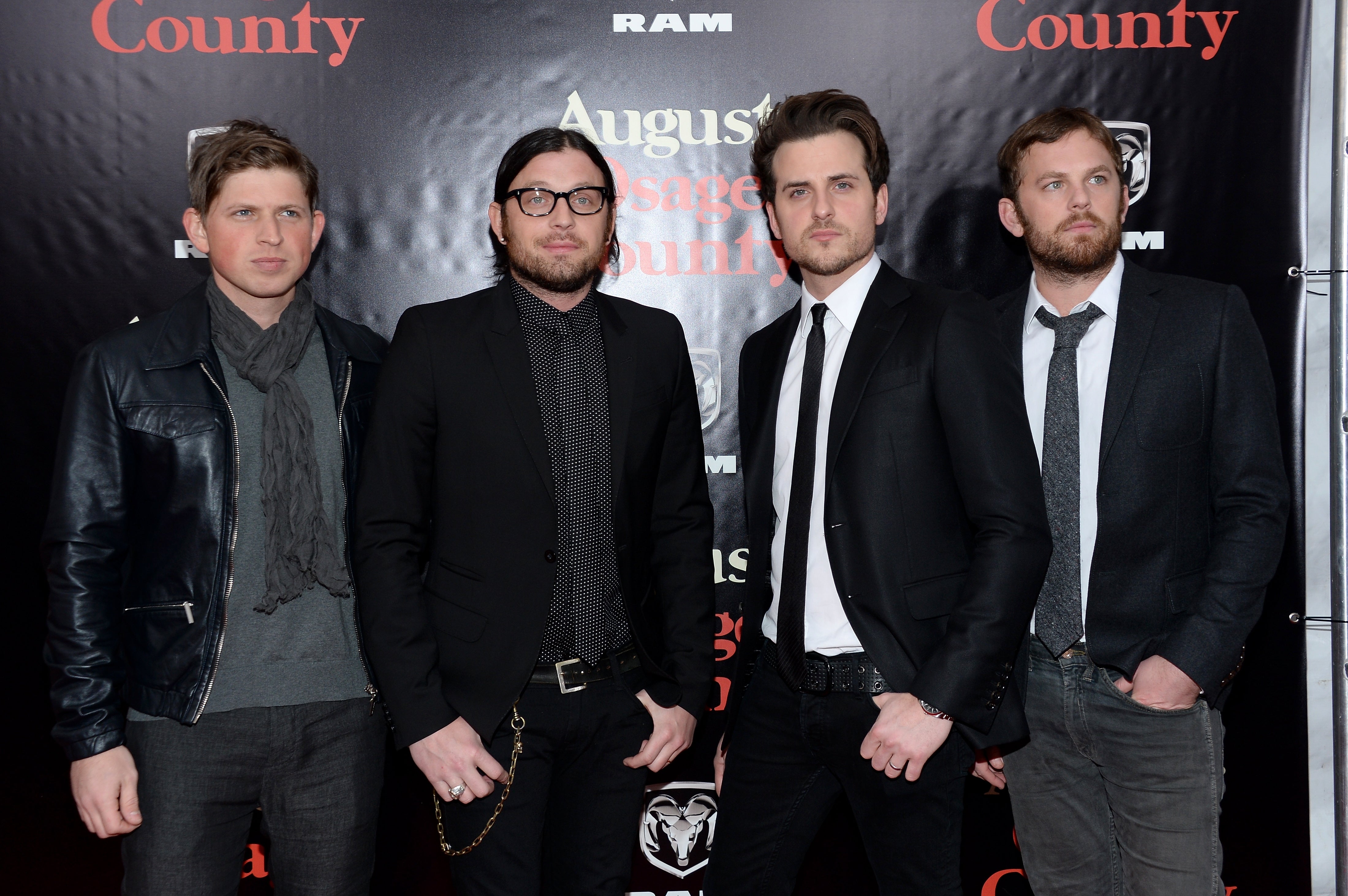 Kings of Leon dressed in stylish suits and casual attire, pose at a red carpet event in front of a backdrop