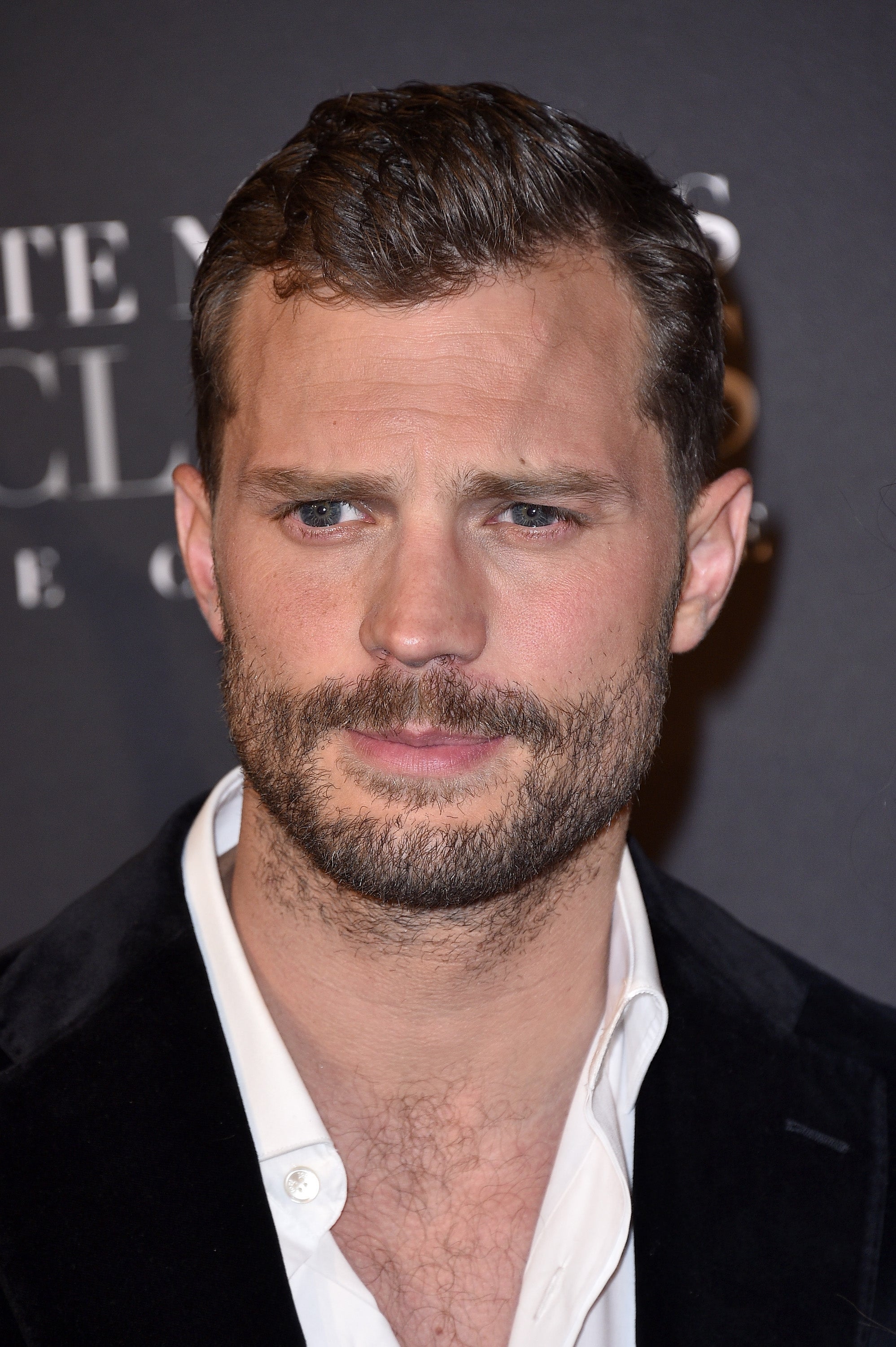 Jamie Dornan with short hair and a beard dressed in a suit jacket and a shirt, posing at a formal event