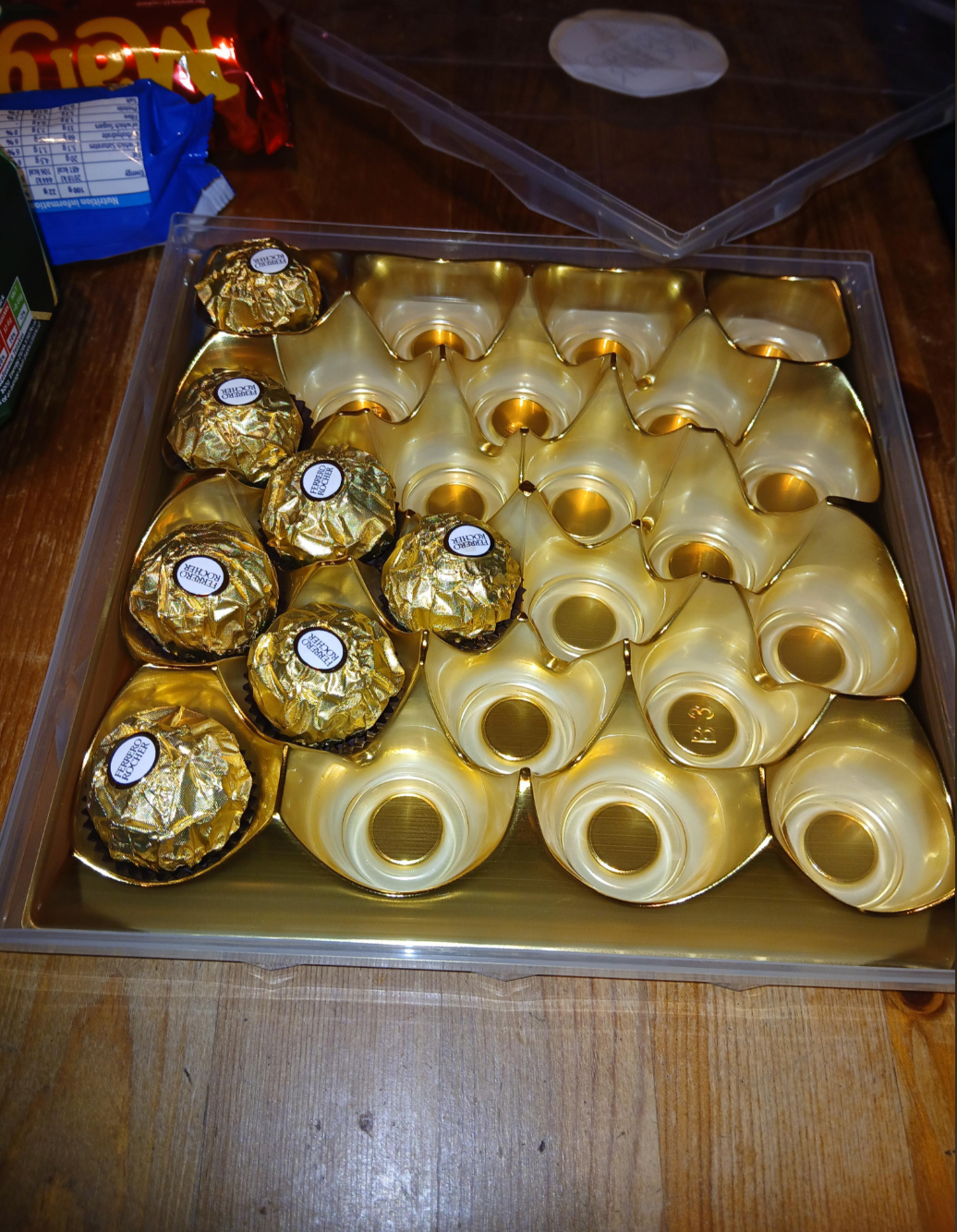 Box of assorted chocolates, some wrapped in foil, with empty spaces indicating missing pieces