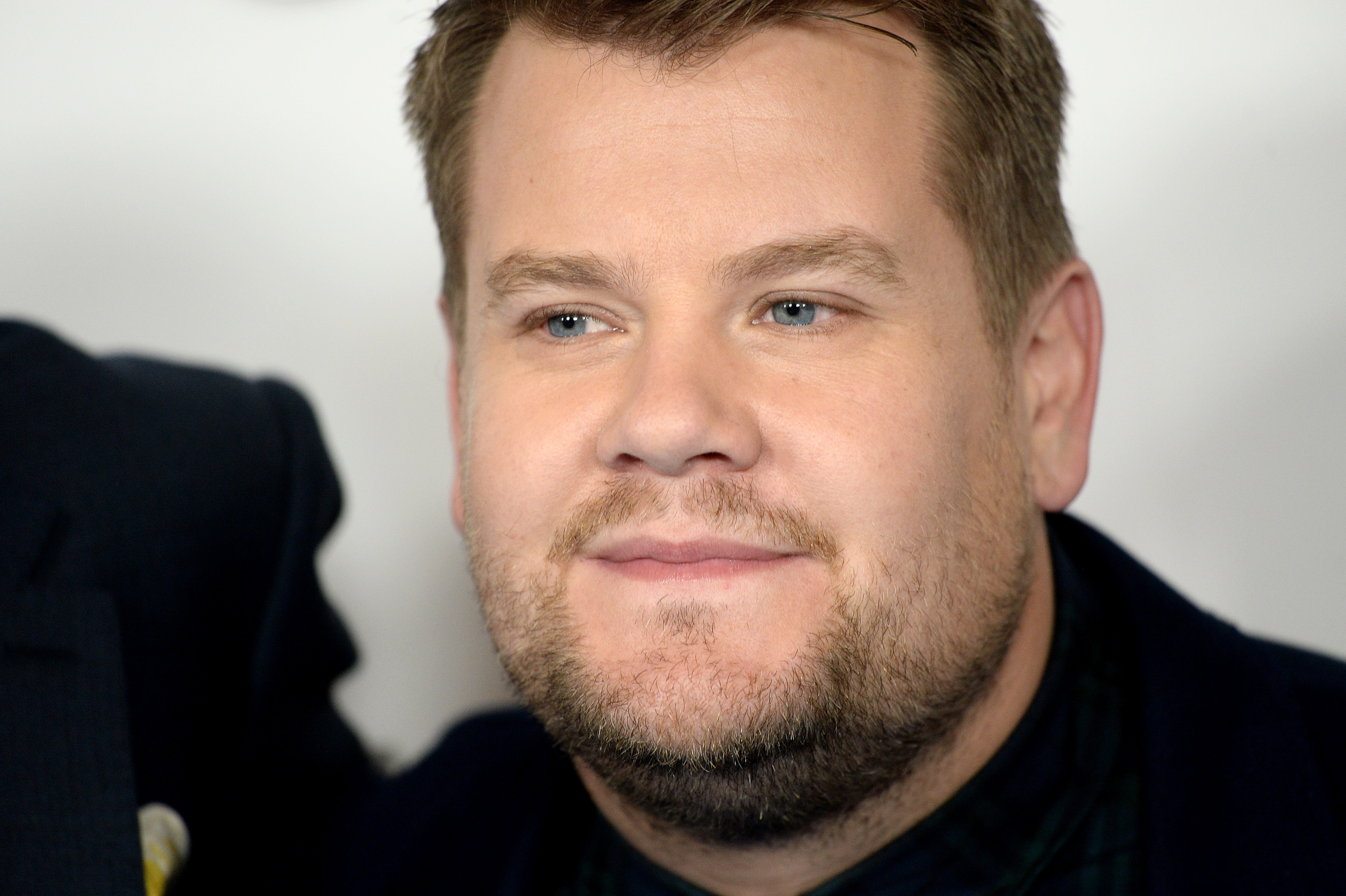 James Corden in a formal outfit on a red carpet, gazing slightly upward with a neutral expression